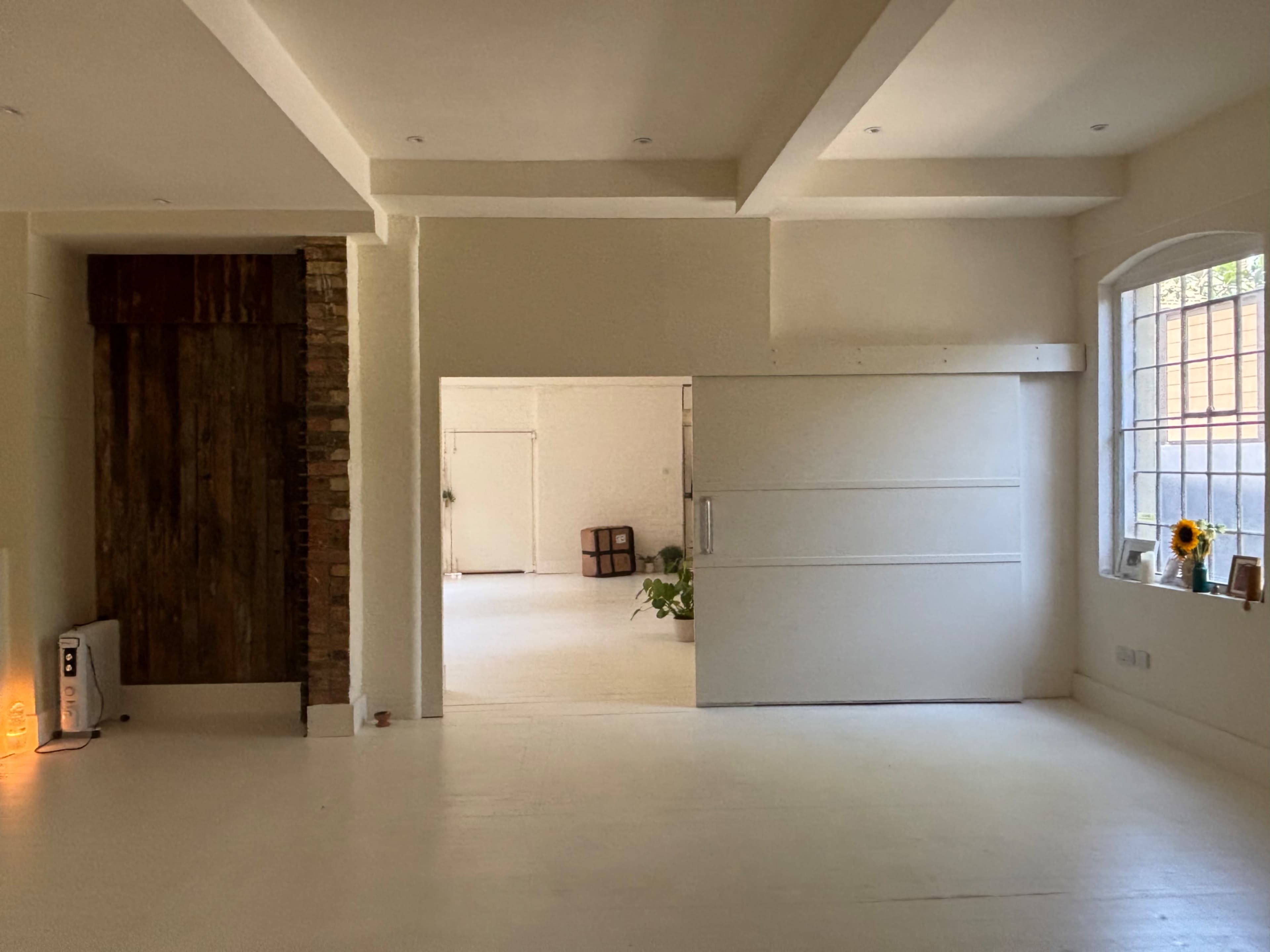 The image shows a spacious, well-lit interior room with a sliding white door, wooden accents, and a few decorative elements.