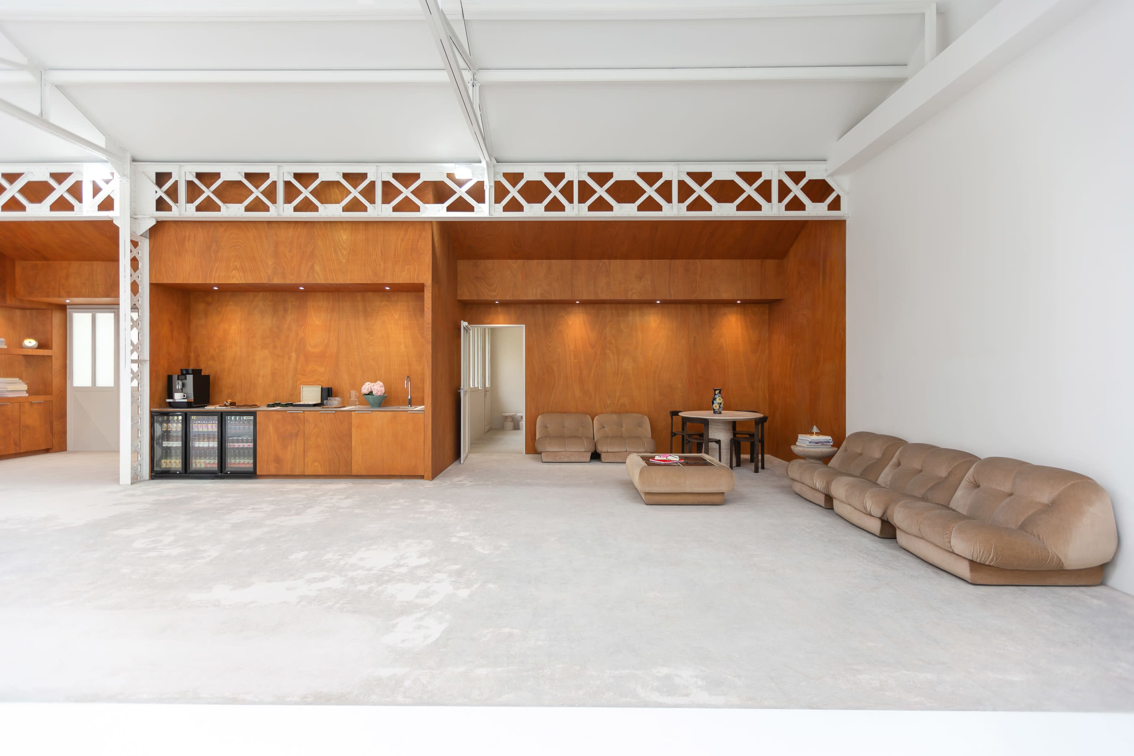The image shows an interior space featuring a spacious living area with a beige couch, a wooden kitchenette, a dining table, and a light-colored floor.