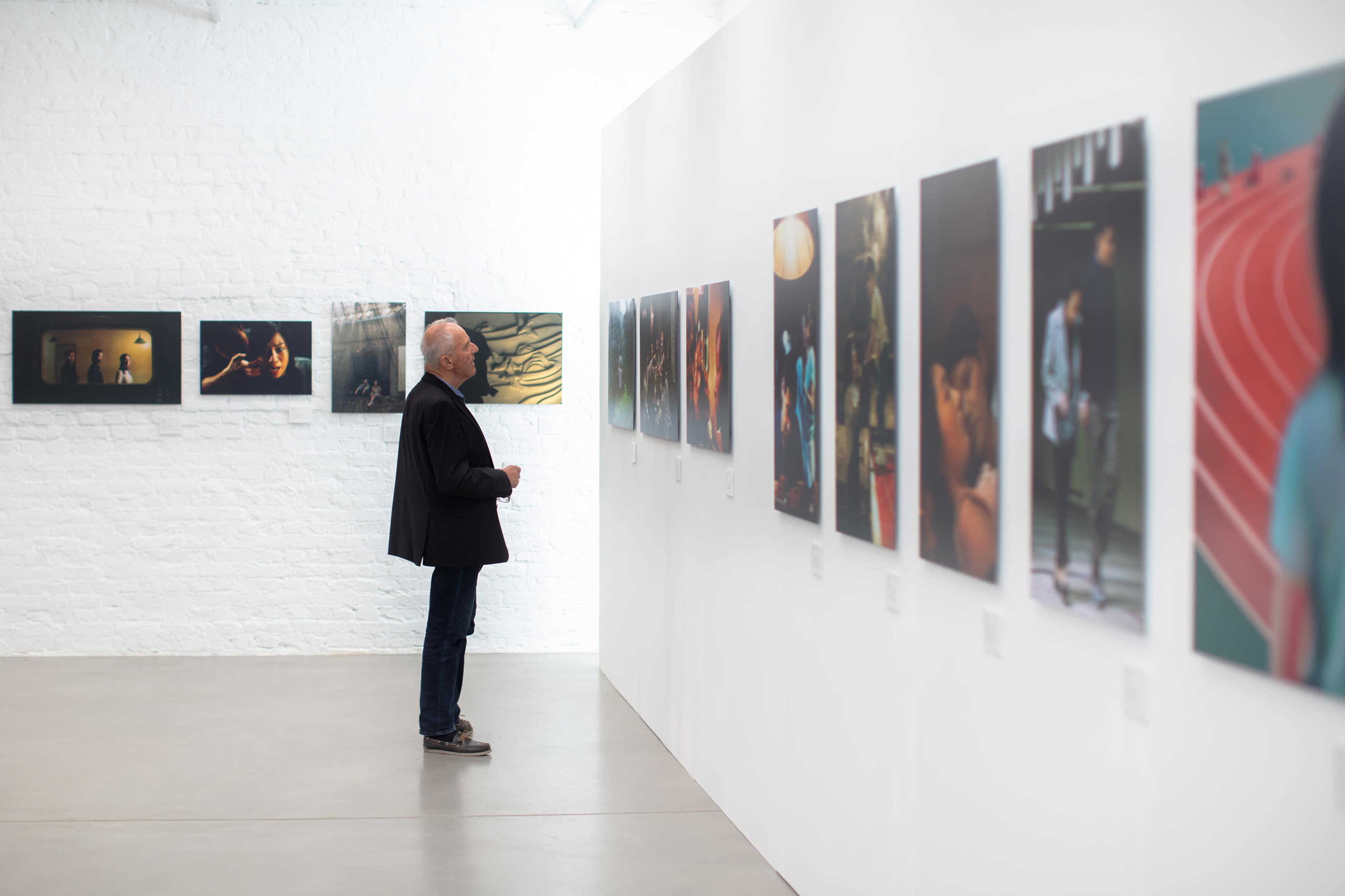 A man stands in an art gallery, observing a series of photographs displayed on white walls.