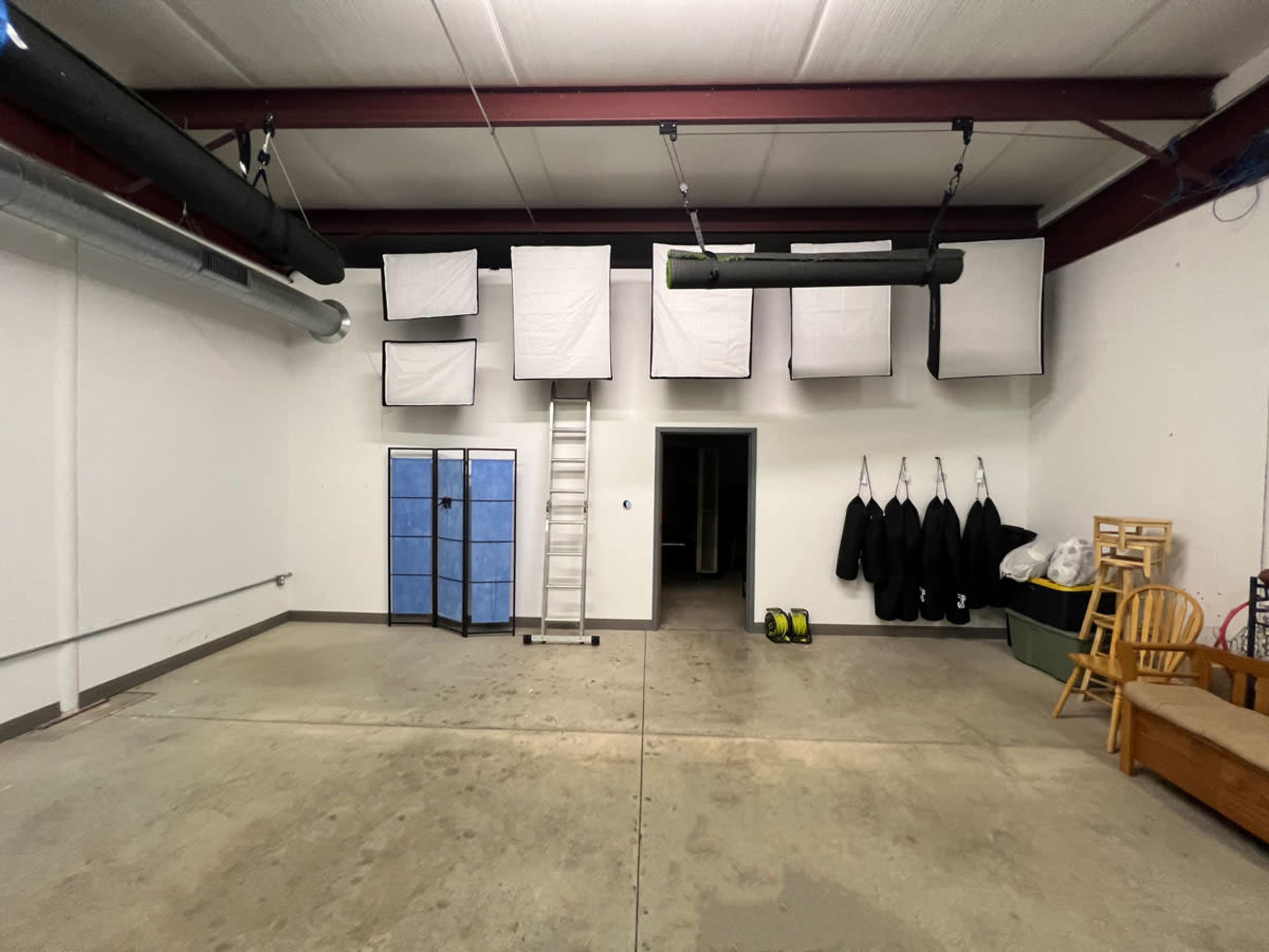 The image shows a spacious garage with a ladder, blue storage unit, and several white fabric boxes hanging from the ceiling.