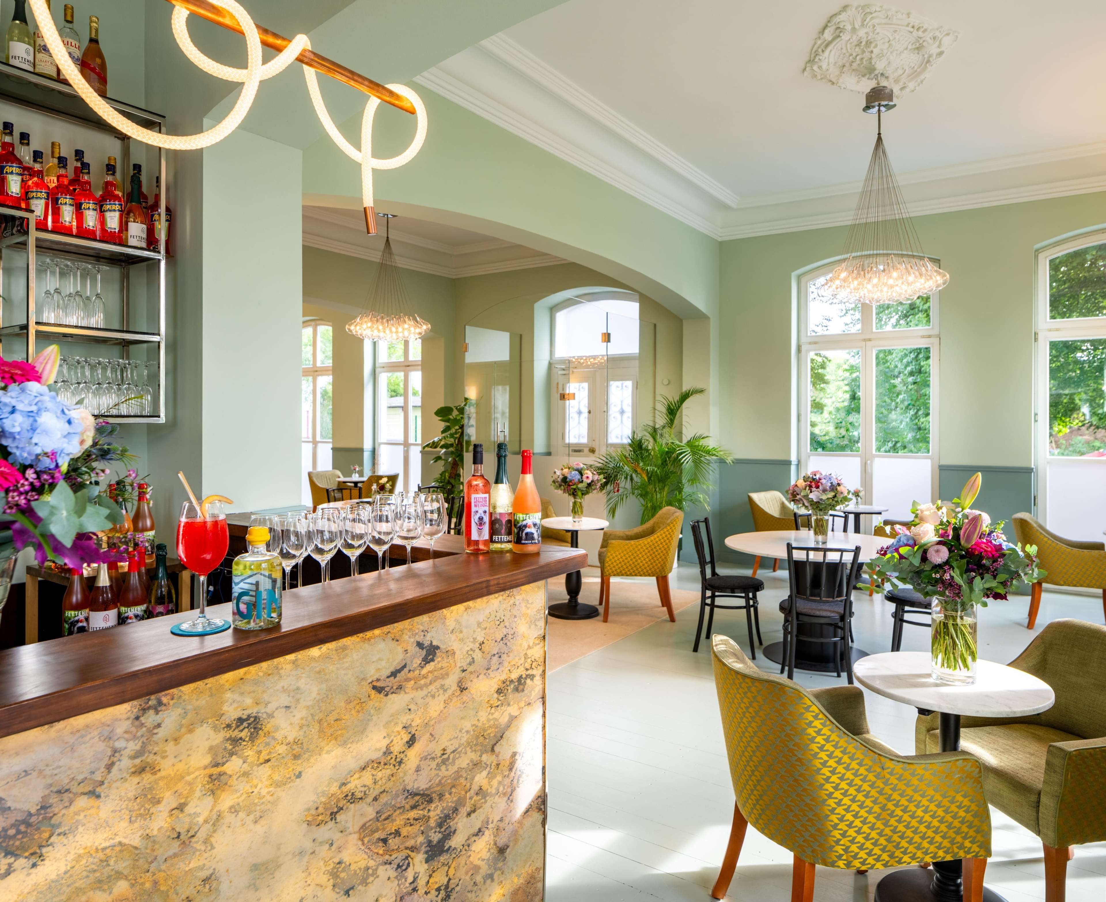 A brightly lit, modern bar area with a variety of drinks on display, surrounded by tables and chairs decorated with flowers.