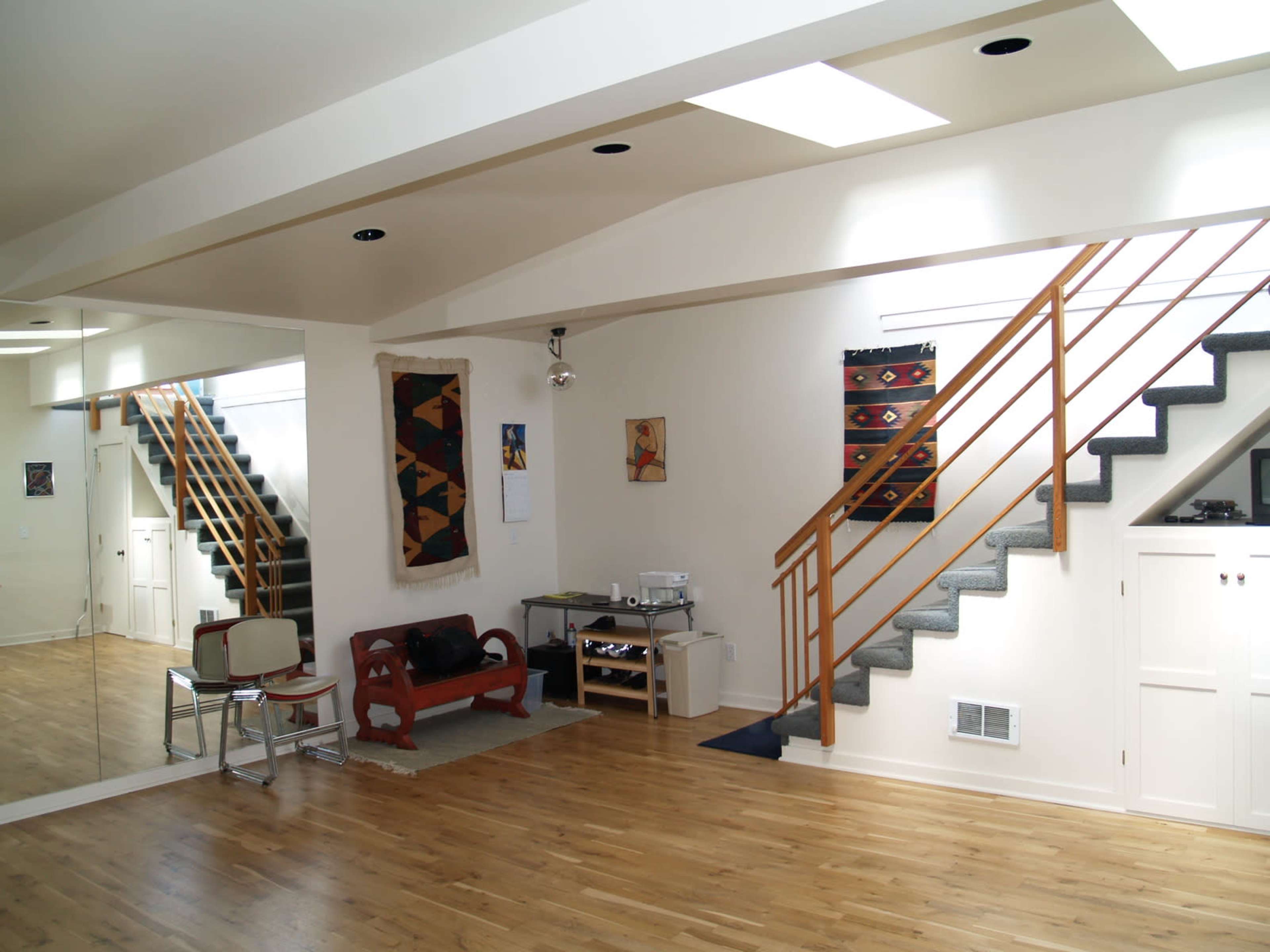 An interior space featuring a wooden floor, a staircase with wooden railings, and a seating area with a chair and small table.