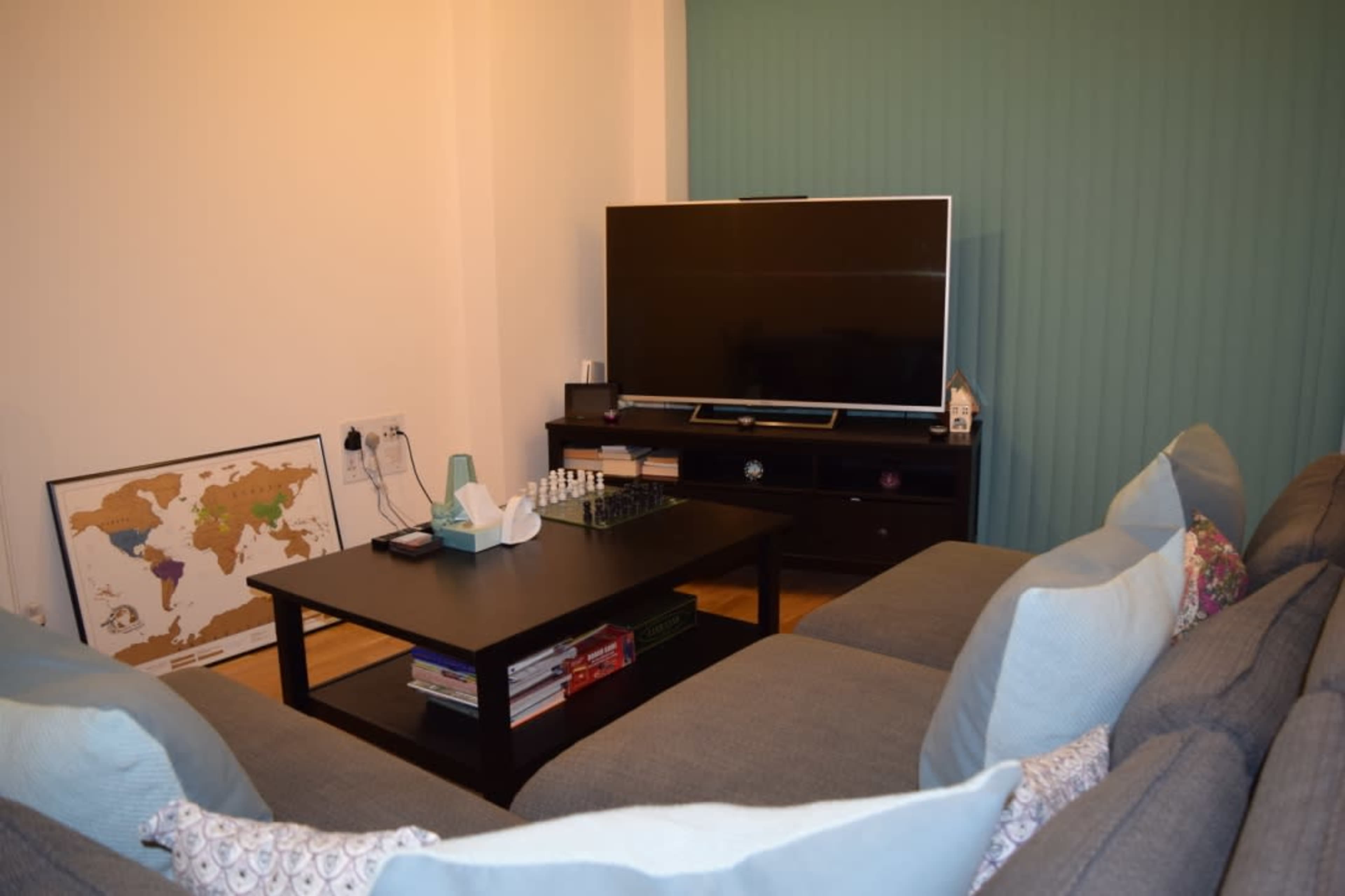 A living room with a gray sofa facing a coffee table, a large television on a stand, and a world map on the wall.
