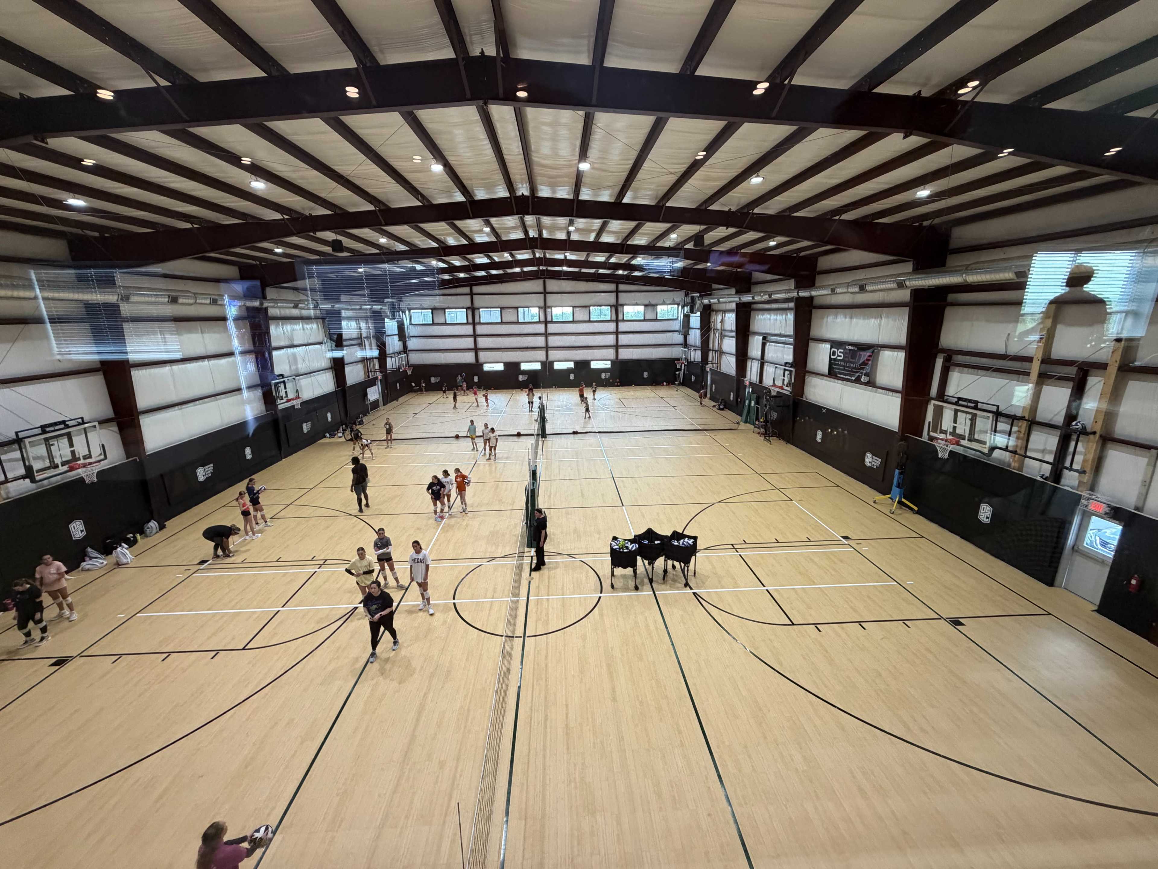 A spacious indoor gymnasium with multiple basketball courts is filled with people participating in various activities.