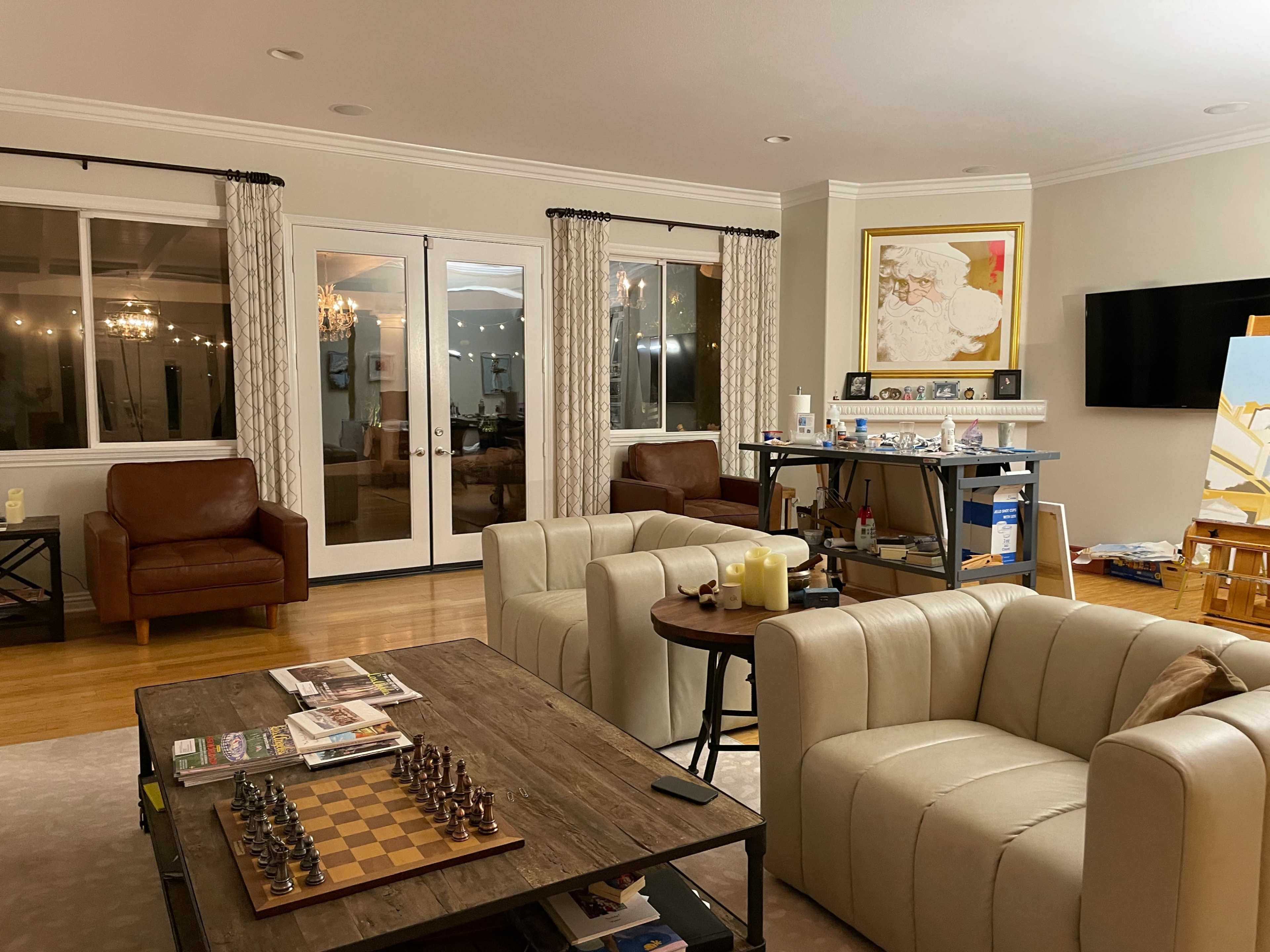 The living room features a coffee table with a chess set, two leather chairs, and an open view to a patio through large glass doors.