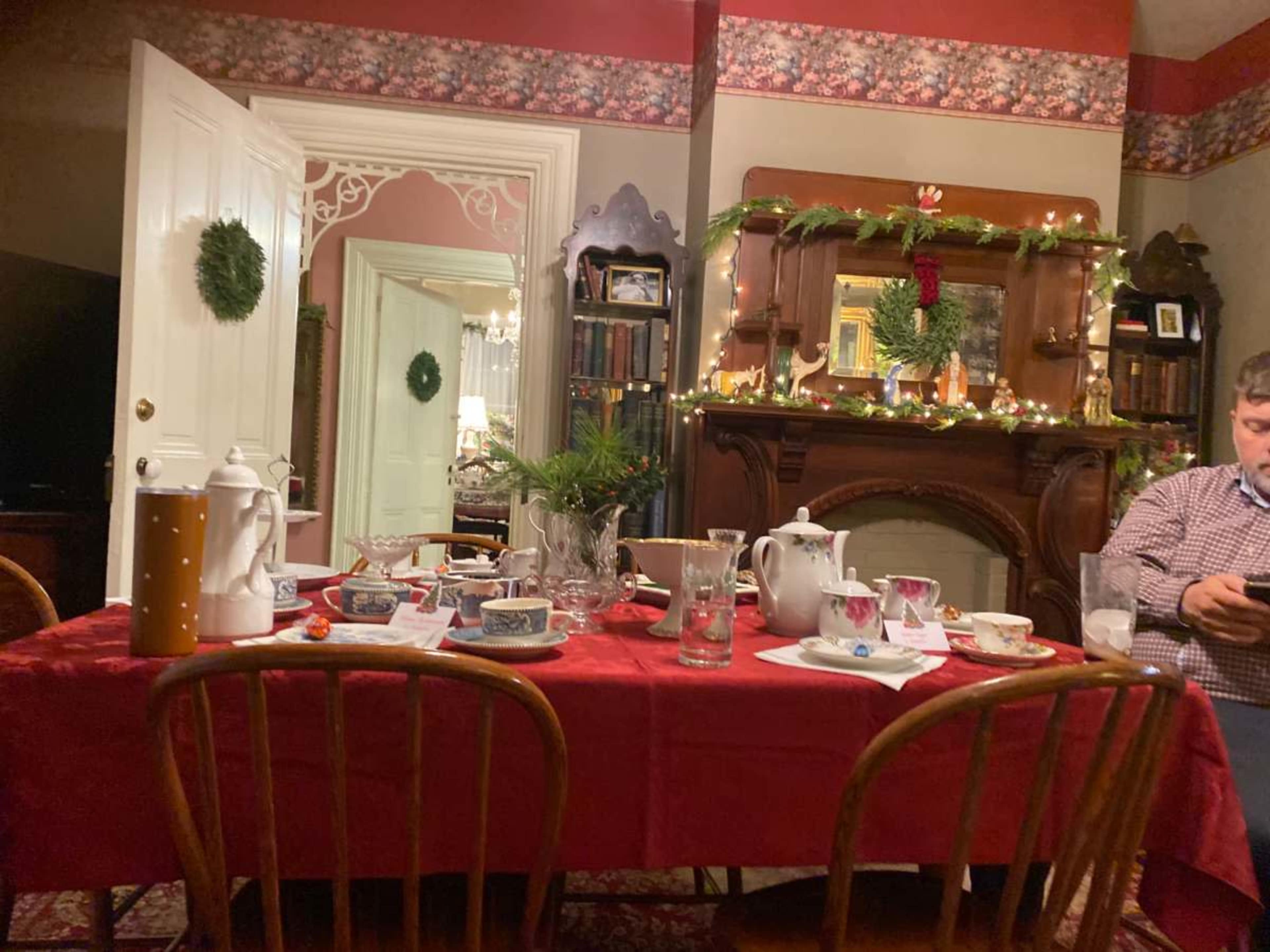 A dining table is set with various dishes and drinks, surrounded by a decorated room featuring a fireplace and seasonal decor.