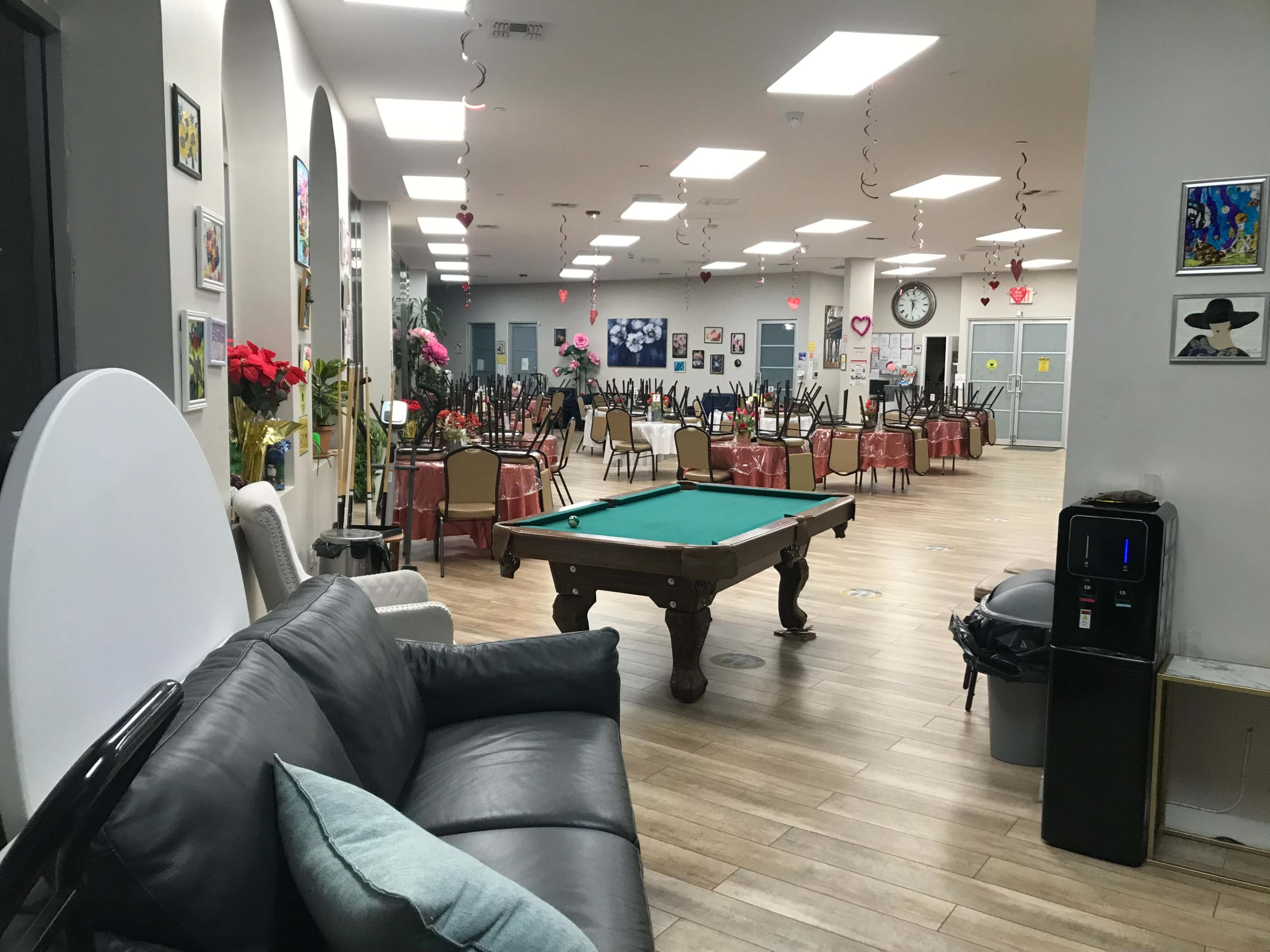 A spacious community hall with a pool table, seating areas, and tables set for dining, adorned with decorations.