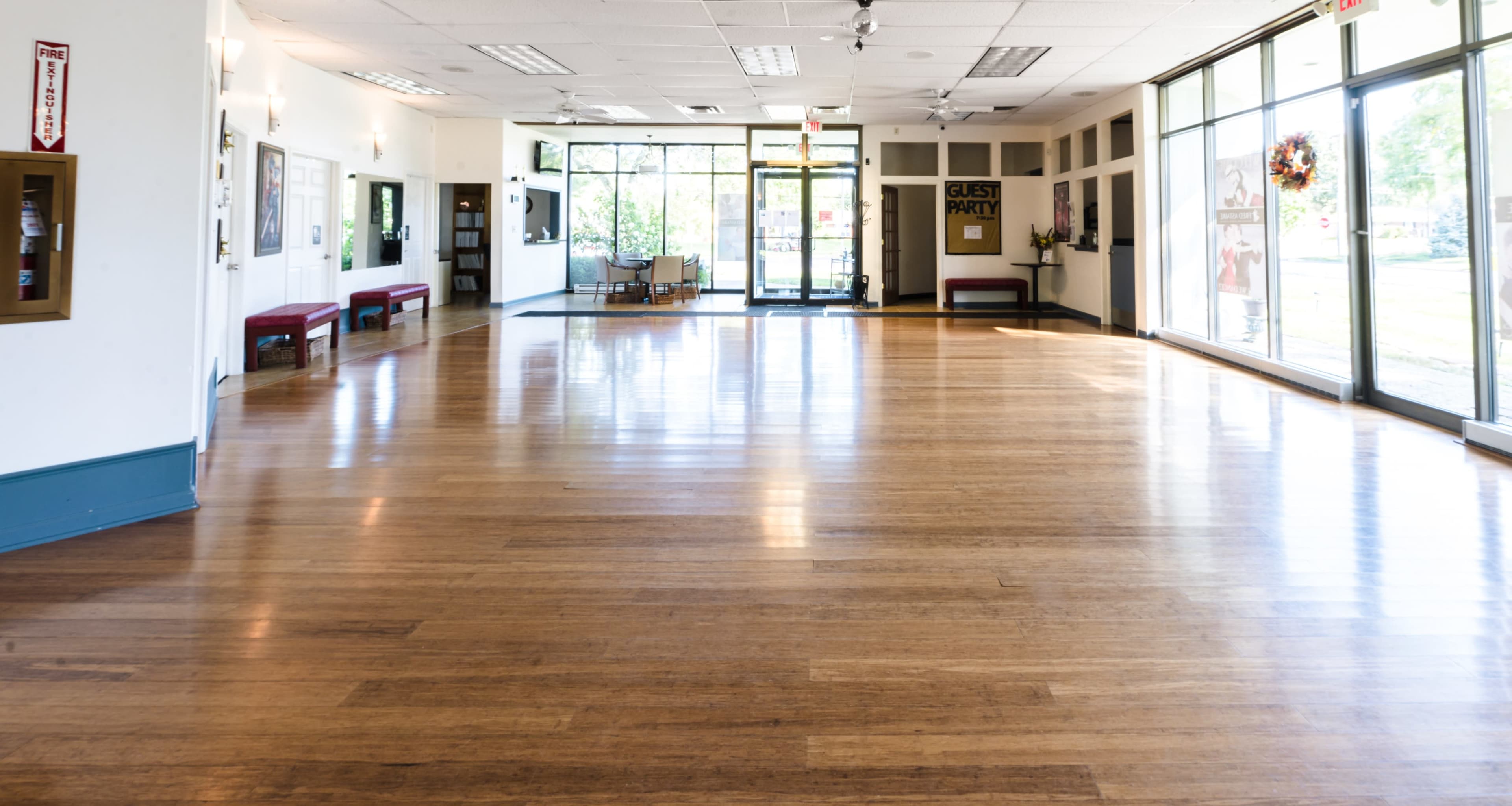 A spacious, empty room with a wooden floor and large windows allowing natural light to enter.