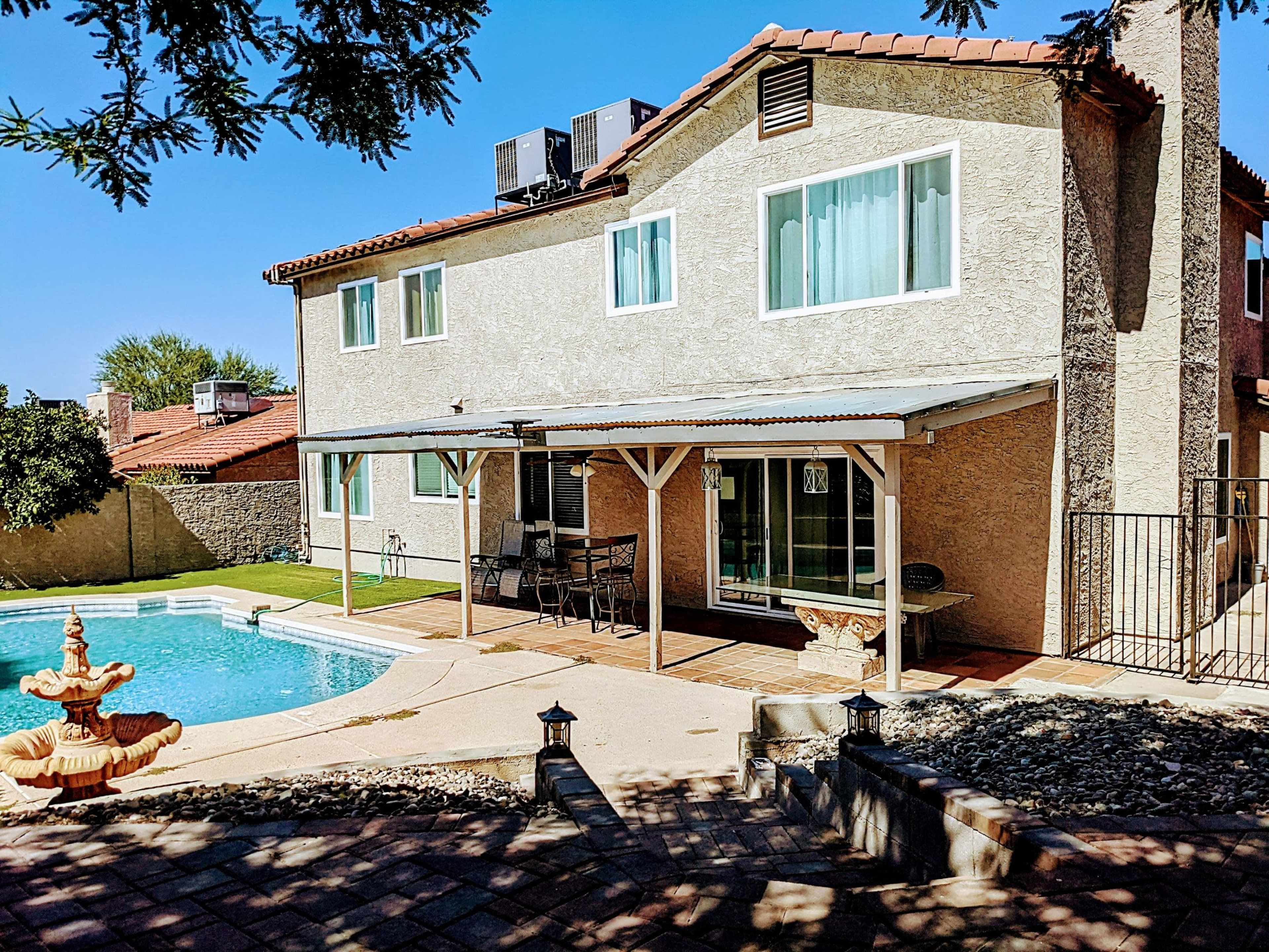 A two-story house with a patio, a swimming pool, and a stone fountain in a backyard setting.