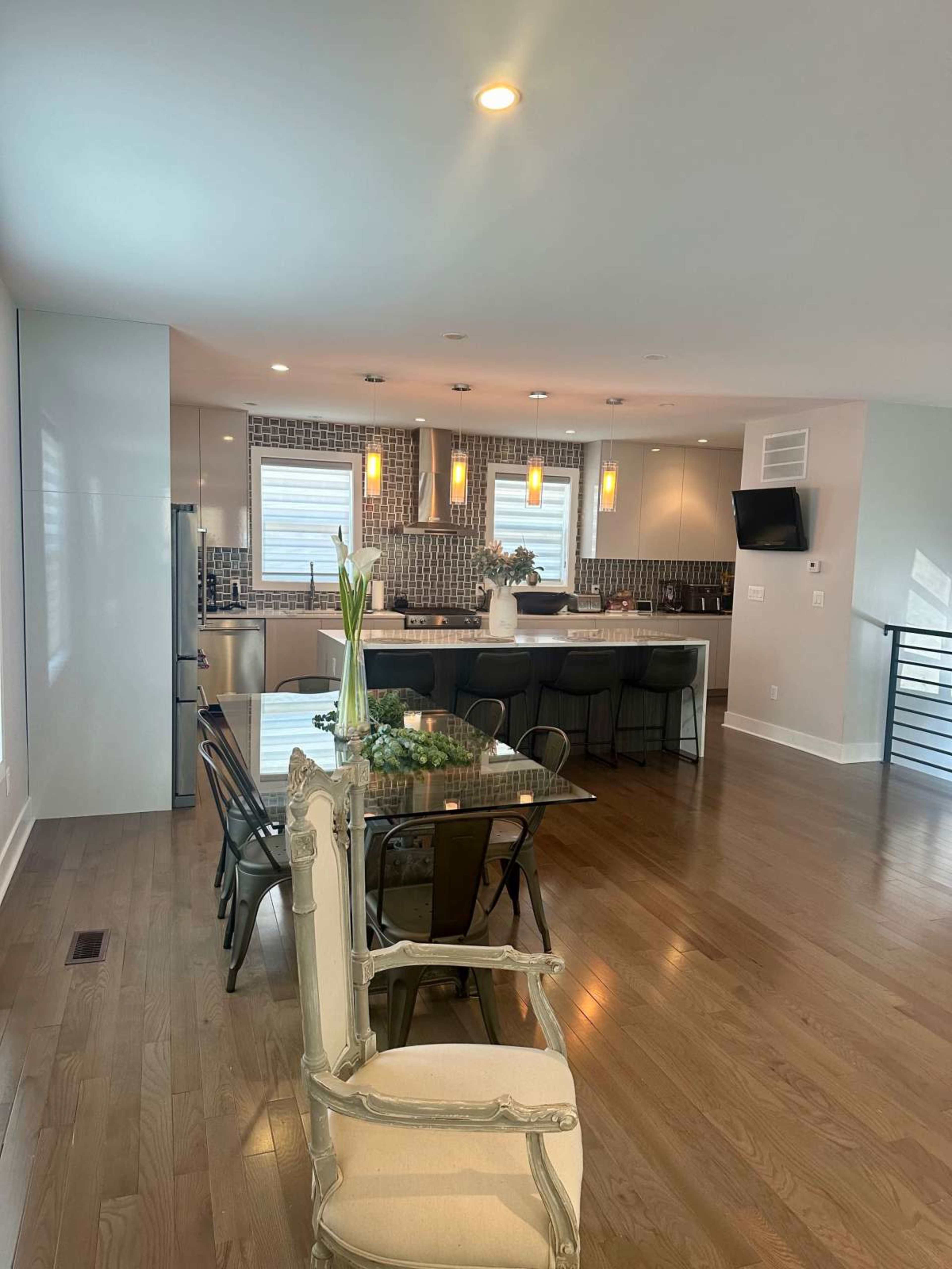 A modern kitchen and dining area with a large wooden table, black chairs, and a well-equipped kitchen featuring a tiled backsplash.