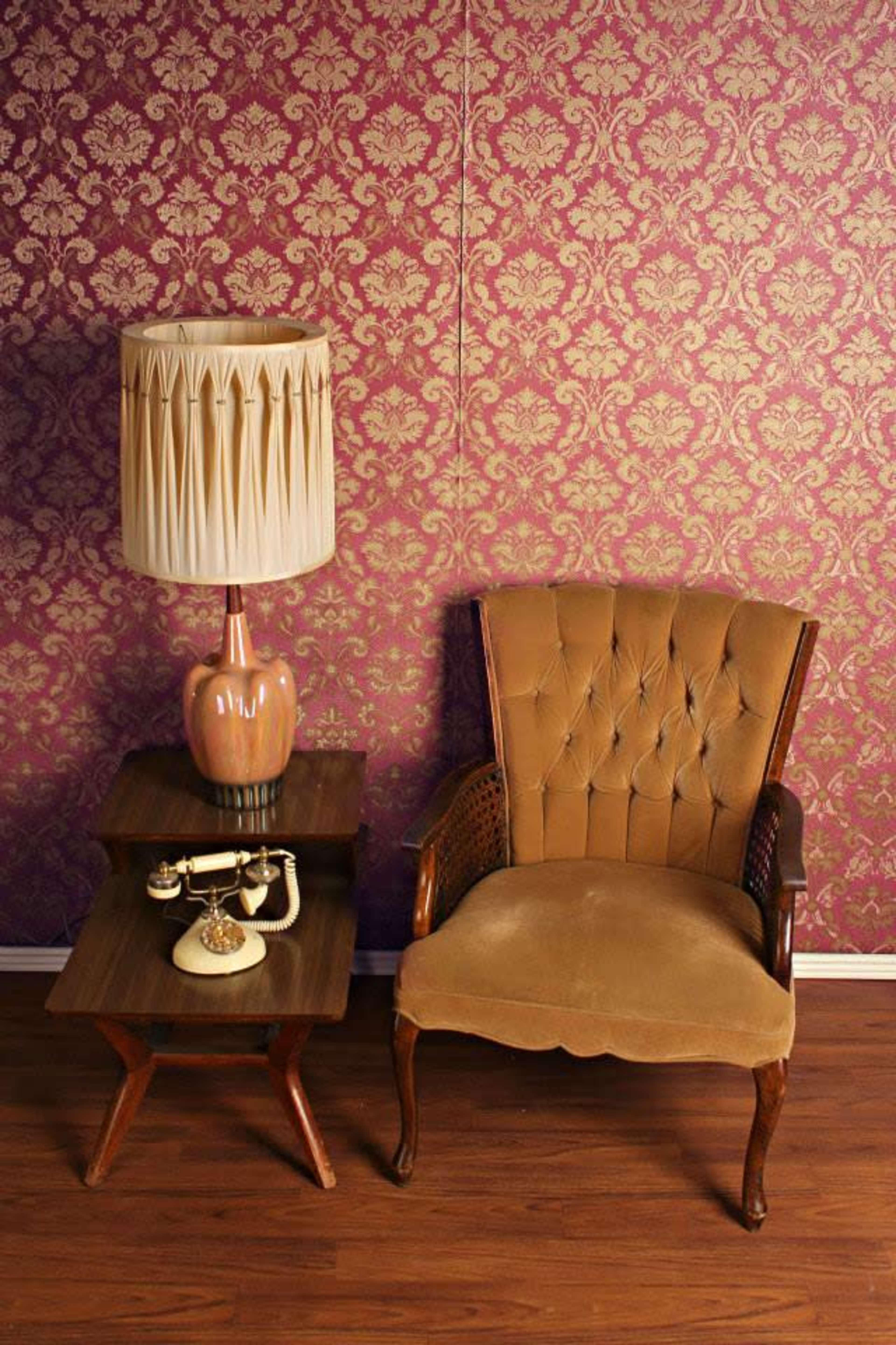 A brown upholstered chair and a small table with a vintage telephone are positioned against a patterned purple wallpaper.