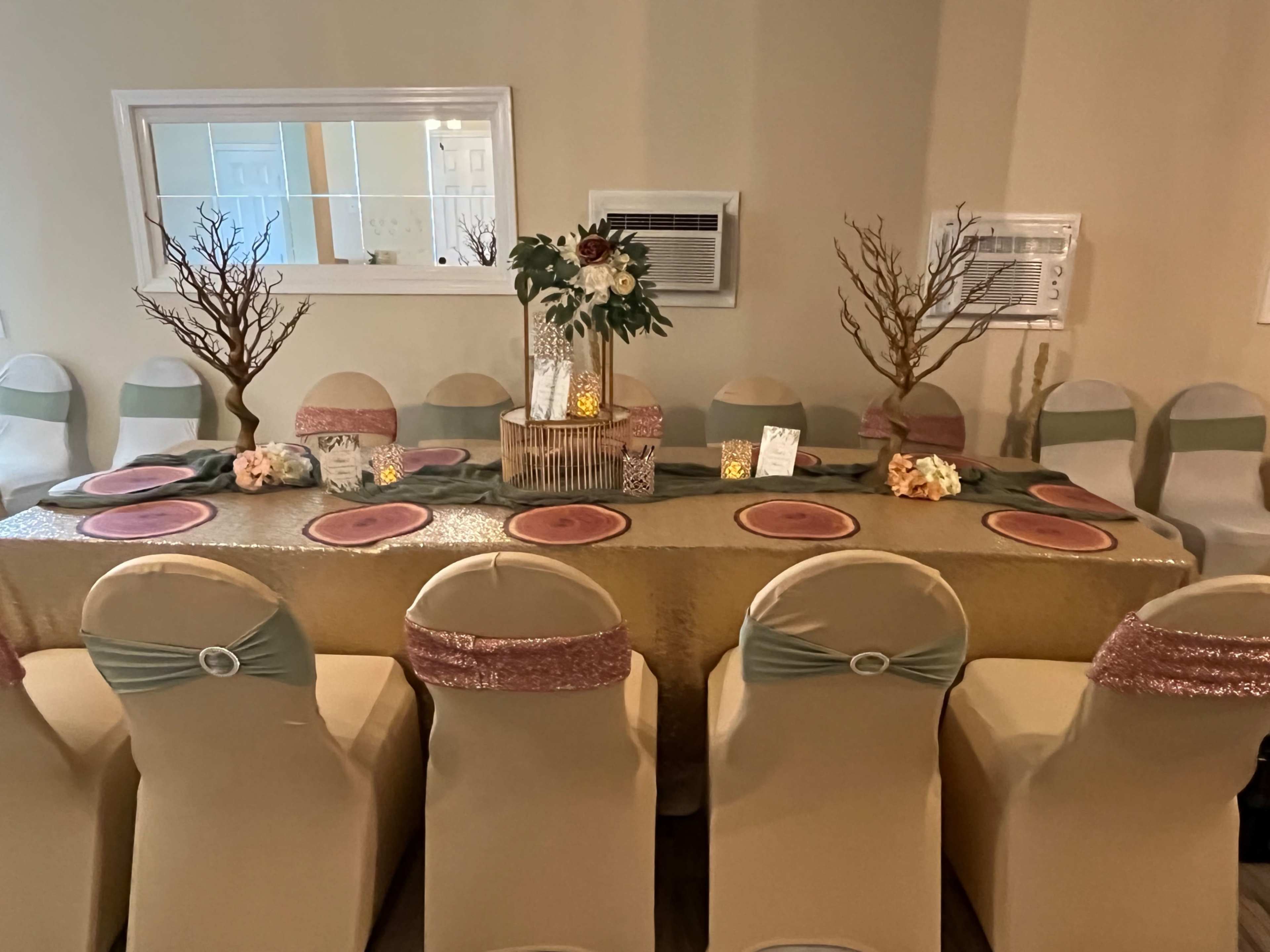 A long banquet table is set with pink and green tableware, surrounded by elegantly draped chairs and adorned with decorative centerpieces.