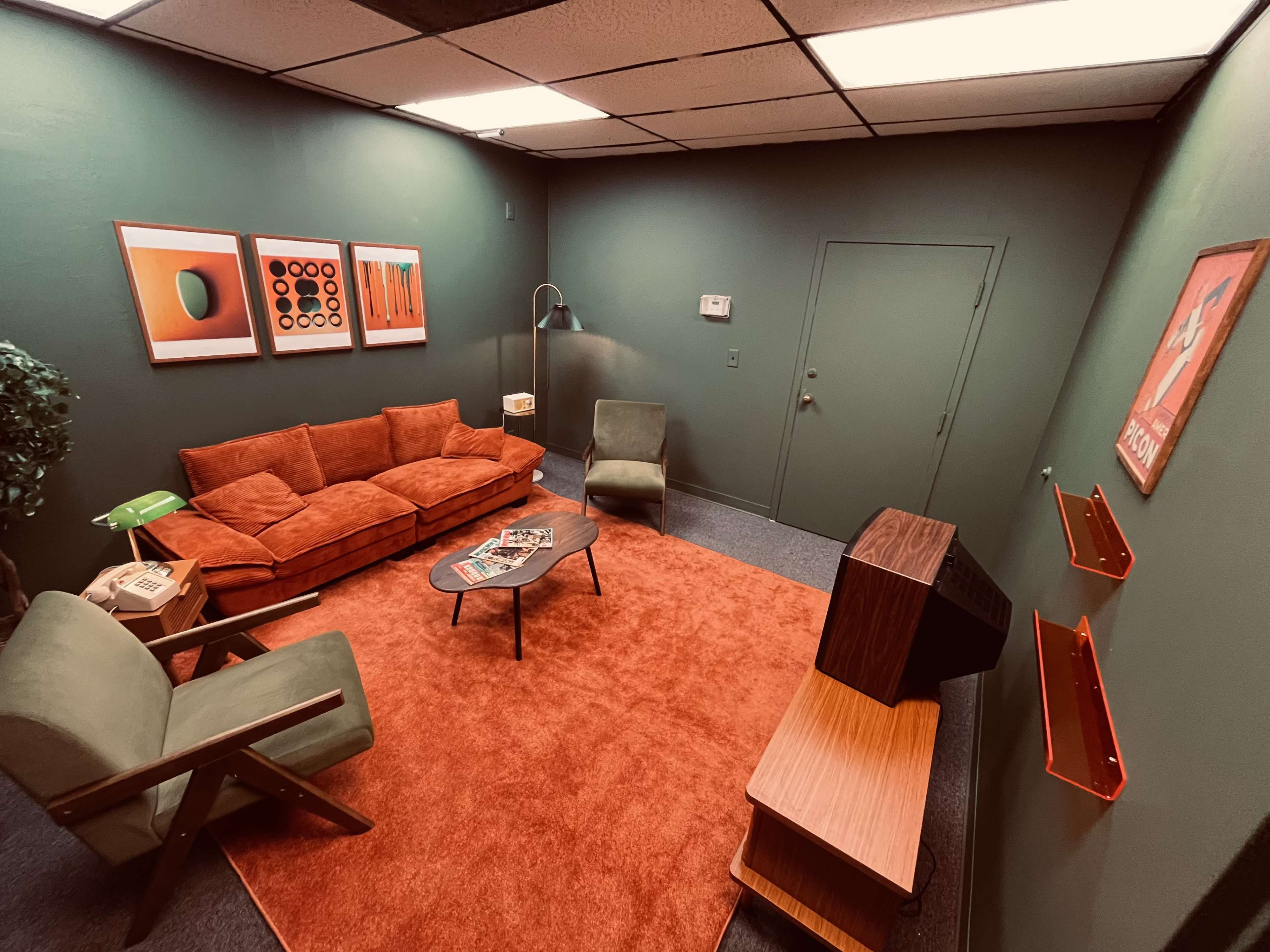 The image depicts a retro-style lounge room with orange and green furnishings, a sofa, an armchair, a coffee table, and a vintage television set.
