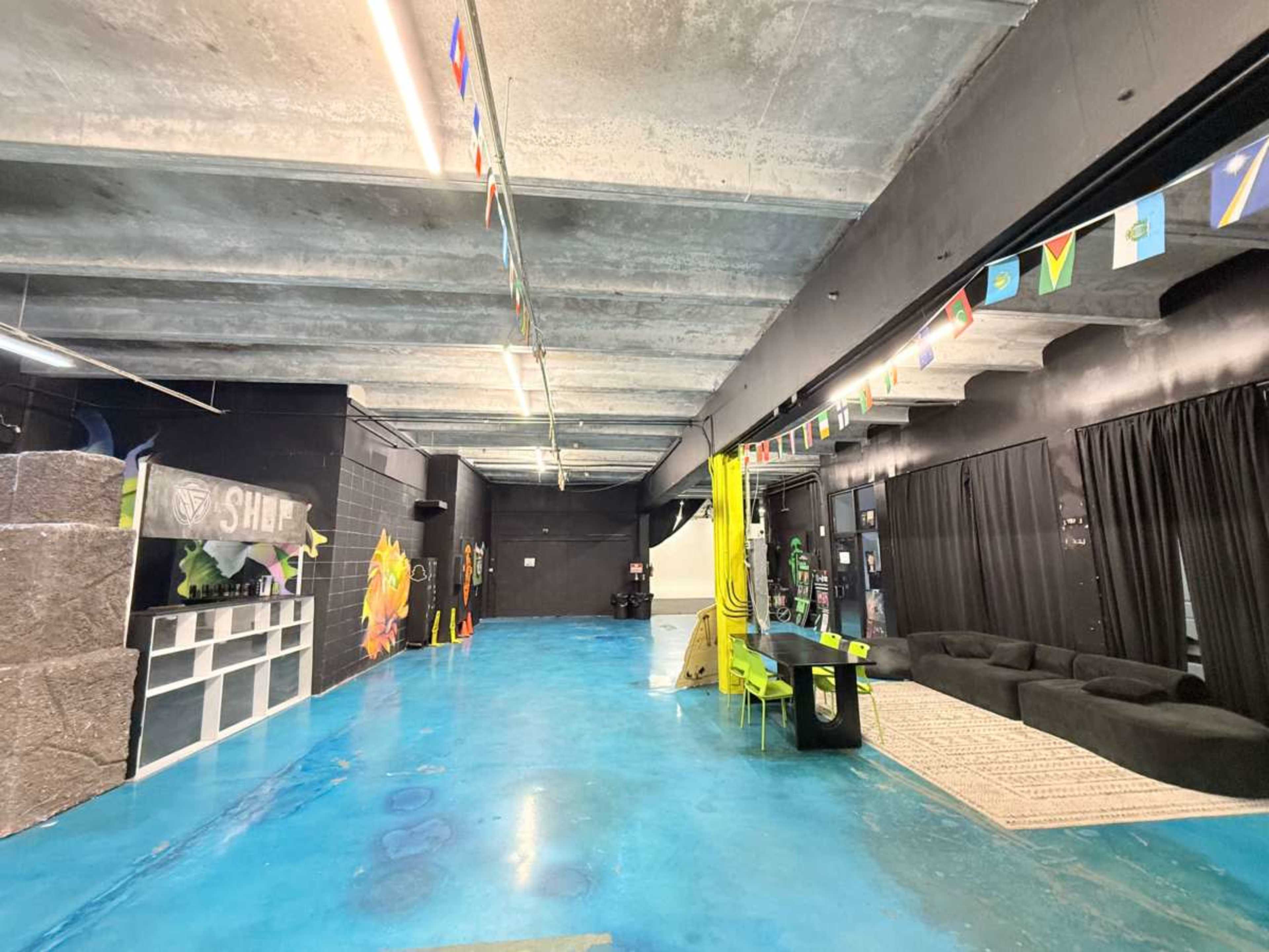The image shows a spacious room with a polished blue floor, featuring black walls, flags hanging from the ceiling, and various furniture elements including a couch and a table.