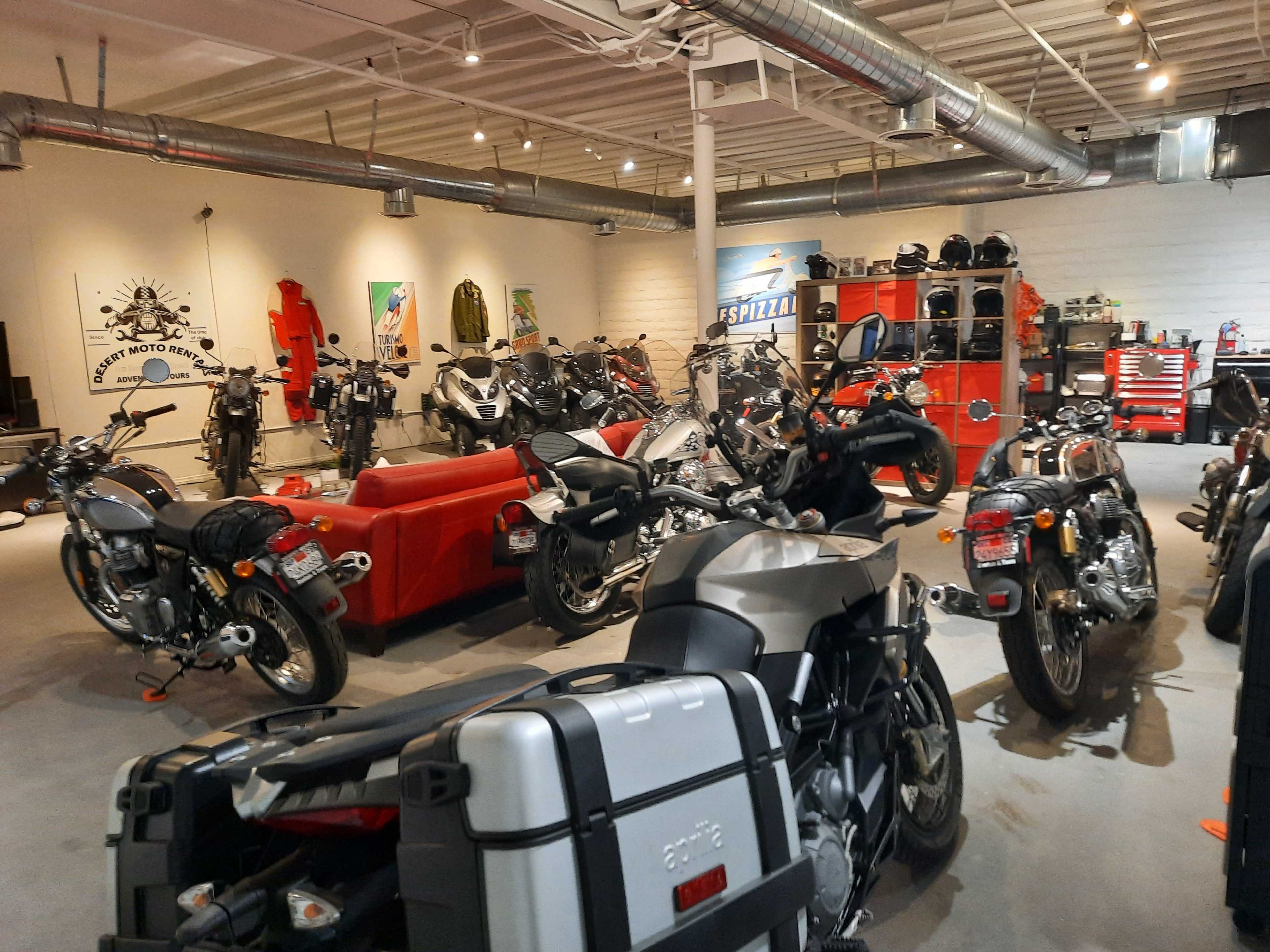 A spacious motorcycle showroom filled with various motorcycle models and accessories, featuring a red couch and tool storage in the background.