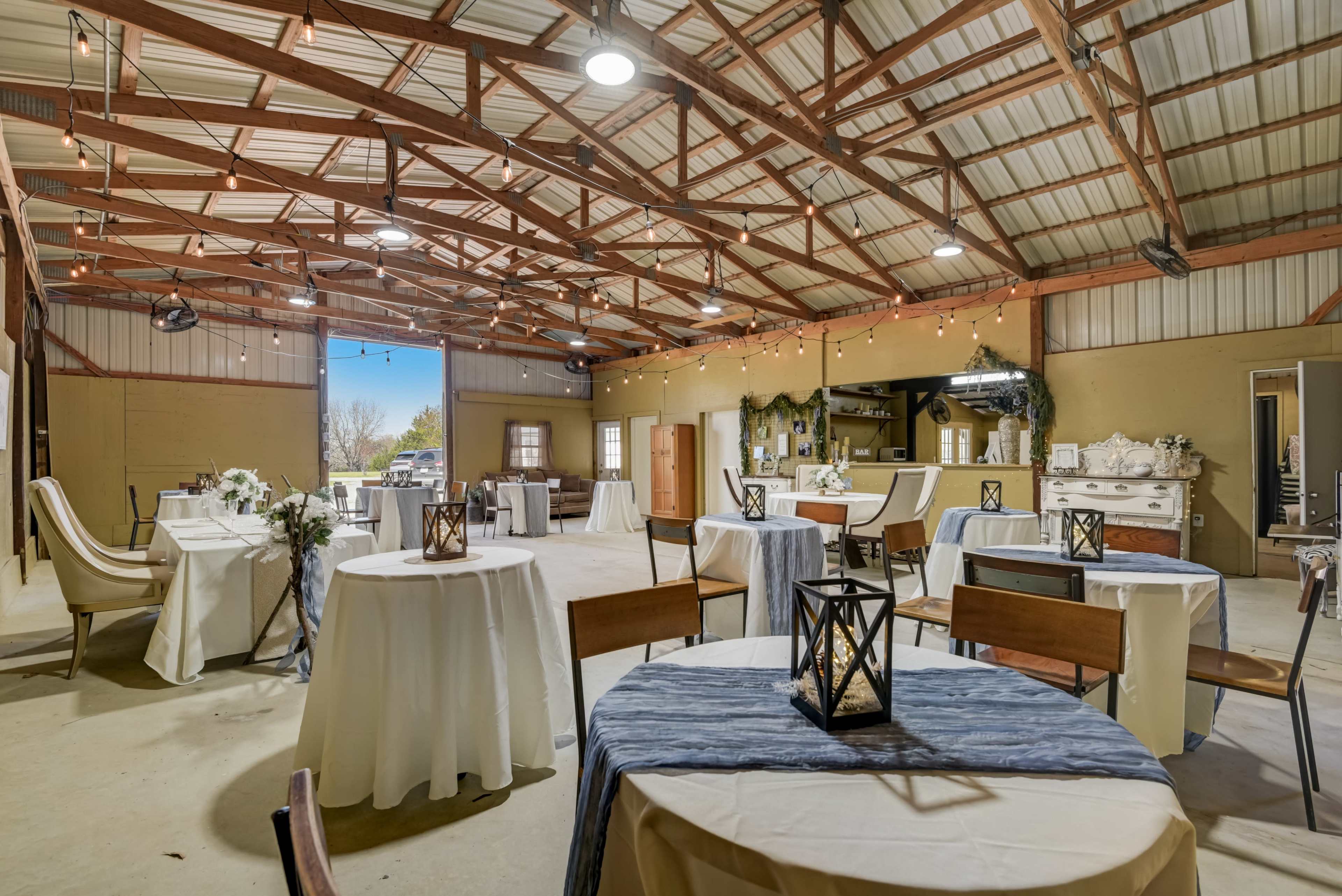 An empty reception hall with round tables, white tablecloths, and decorative lanterns under a vaulted ceiling.