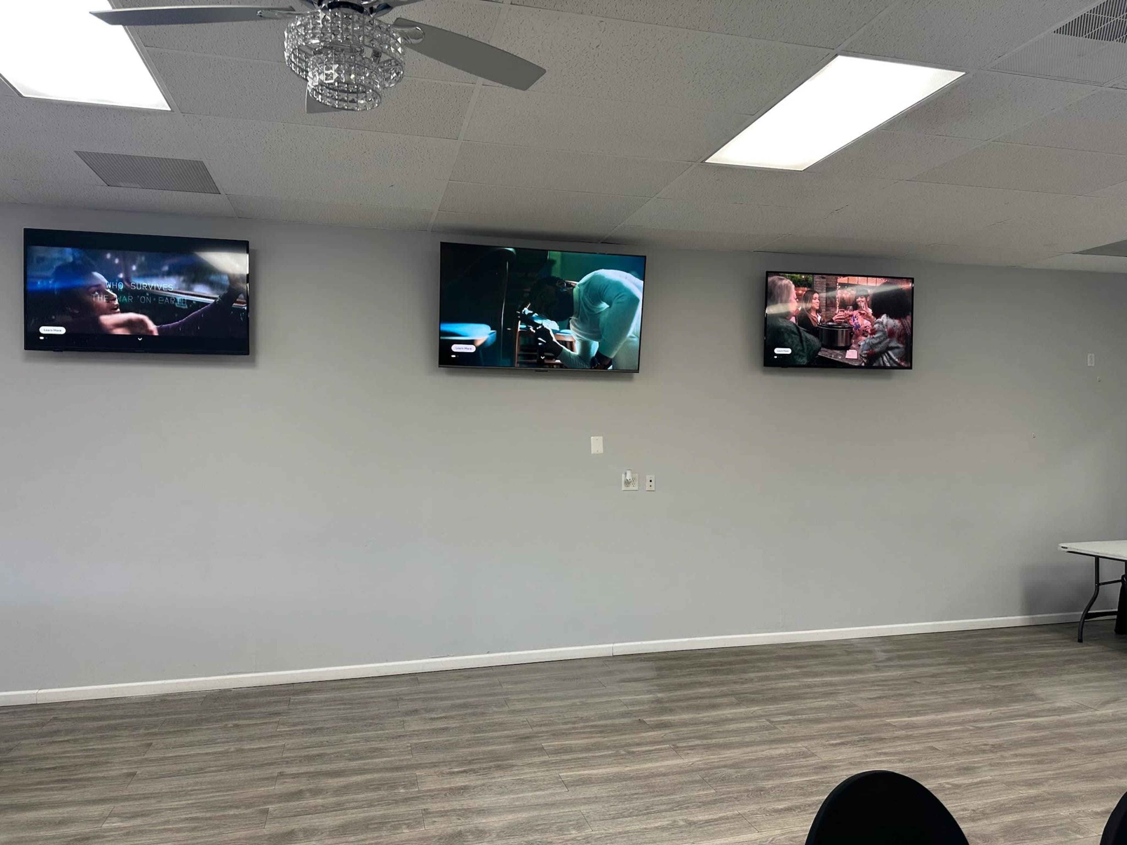 Three television screens are mounted on a light gray wall, each displaying different scenes from various shows or movies.