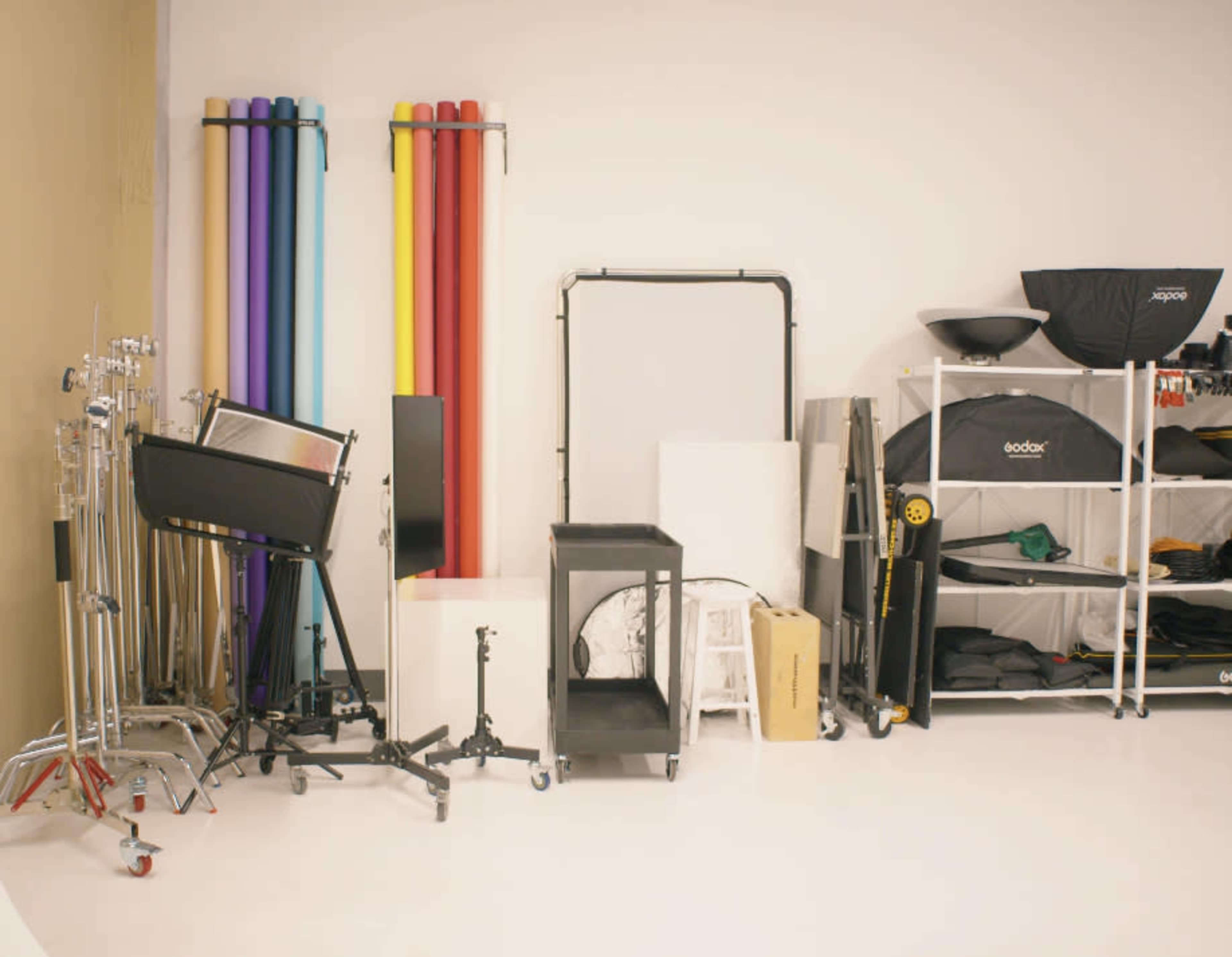 The image shows a photography studio setup with various backdrops, lighting equipment, and storage shelves.