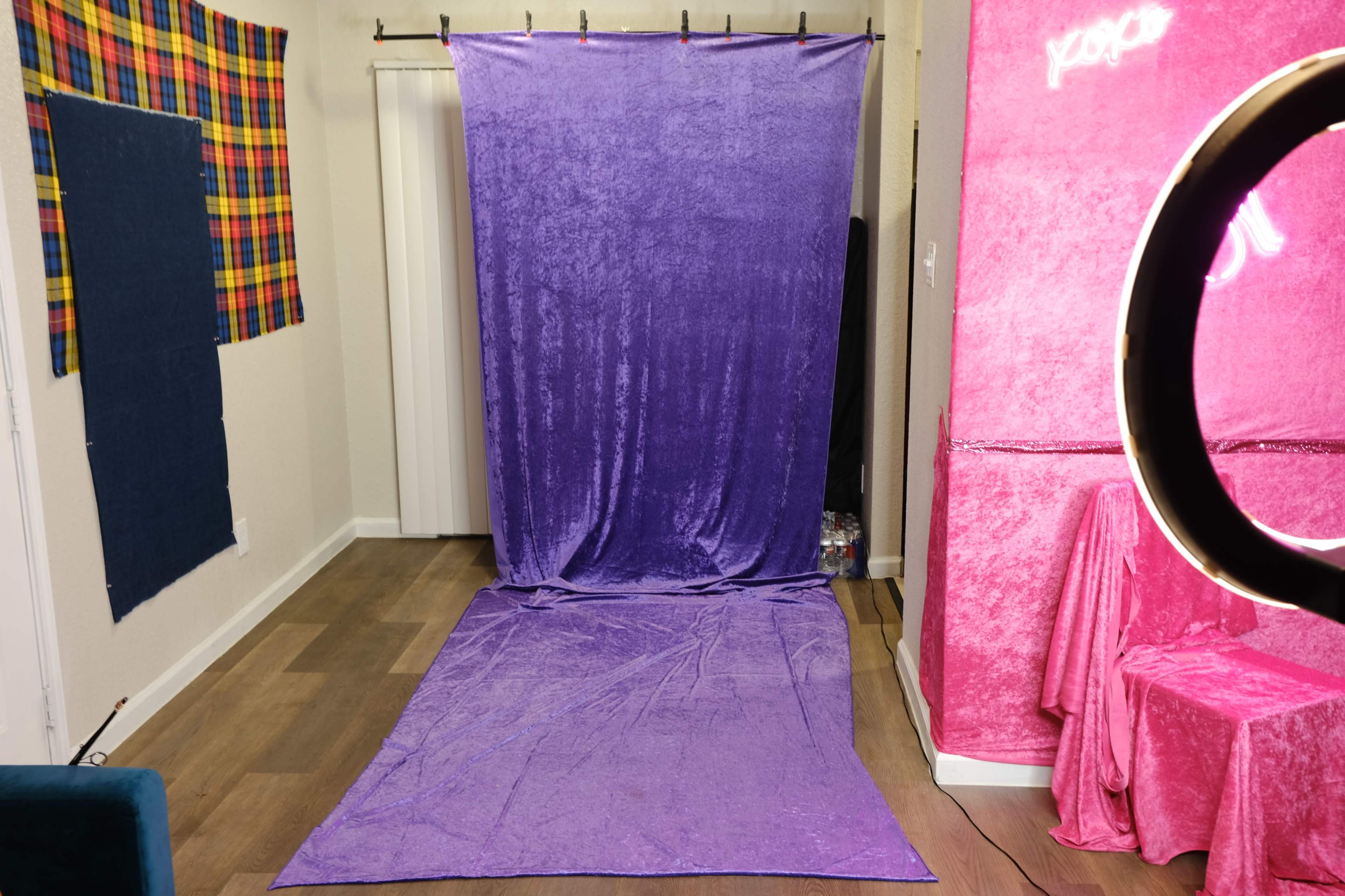 A small indoor space featuring a purple backdrop hanging from a rod, with a matching purple floor covering, and pink draped fabric visible on the right side.