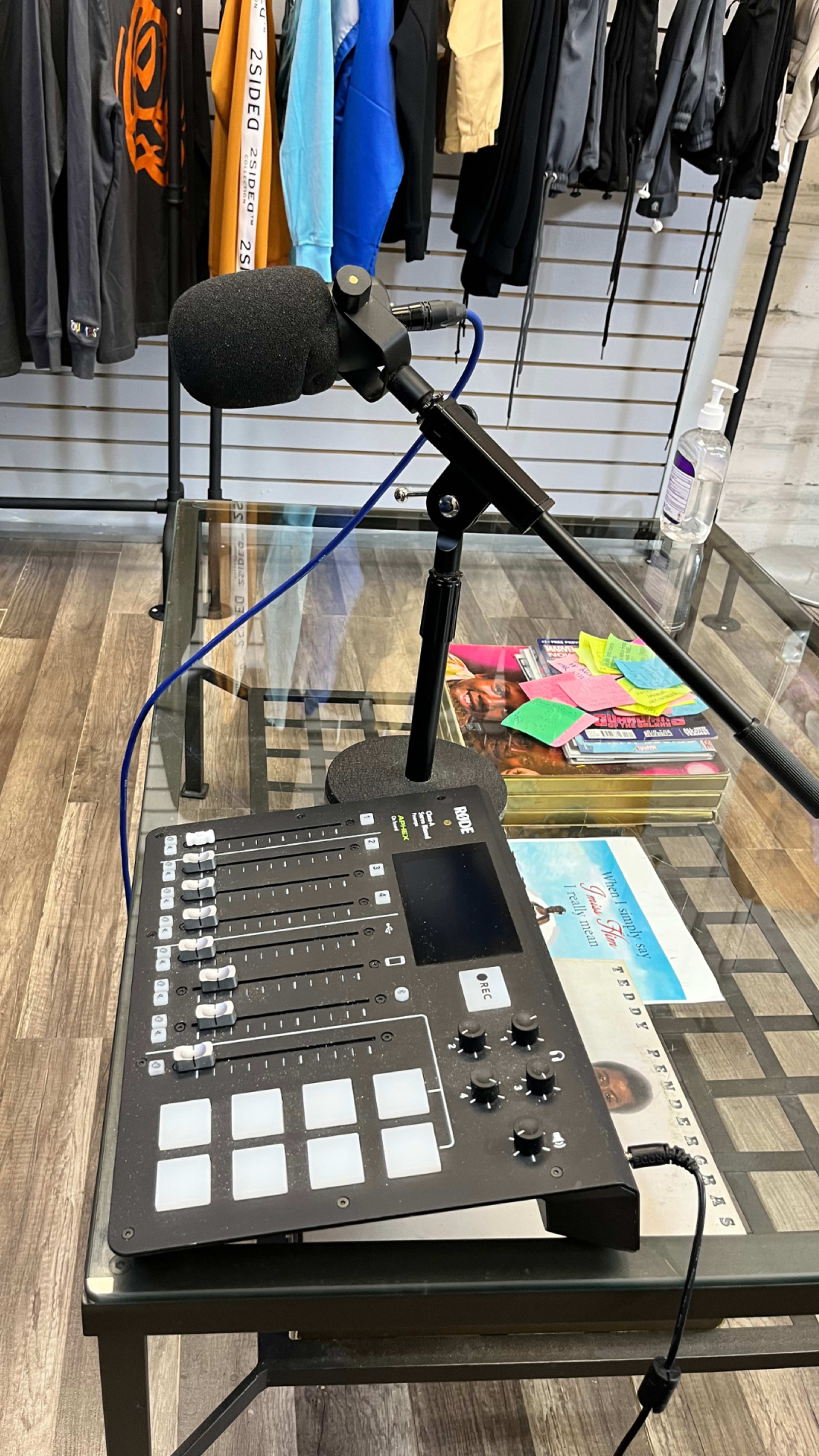A microphone is positioned on a stand next to a sound mixing device on a glass table in a shop.