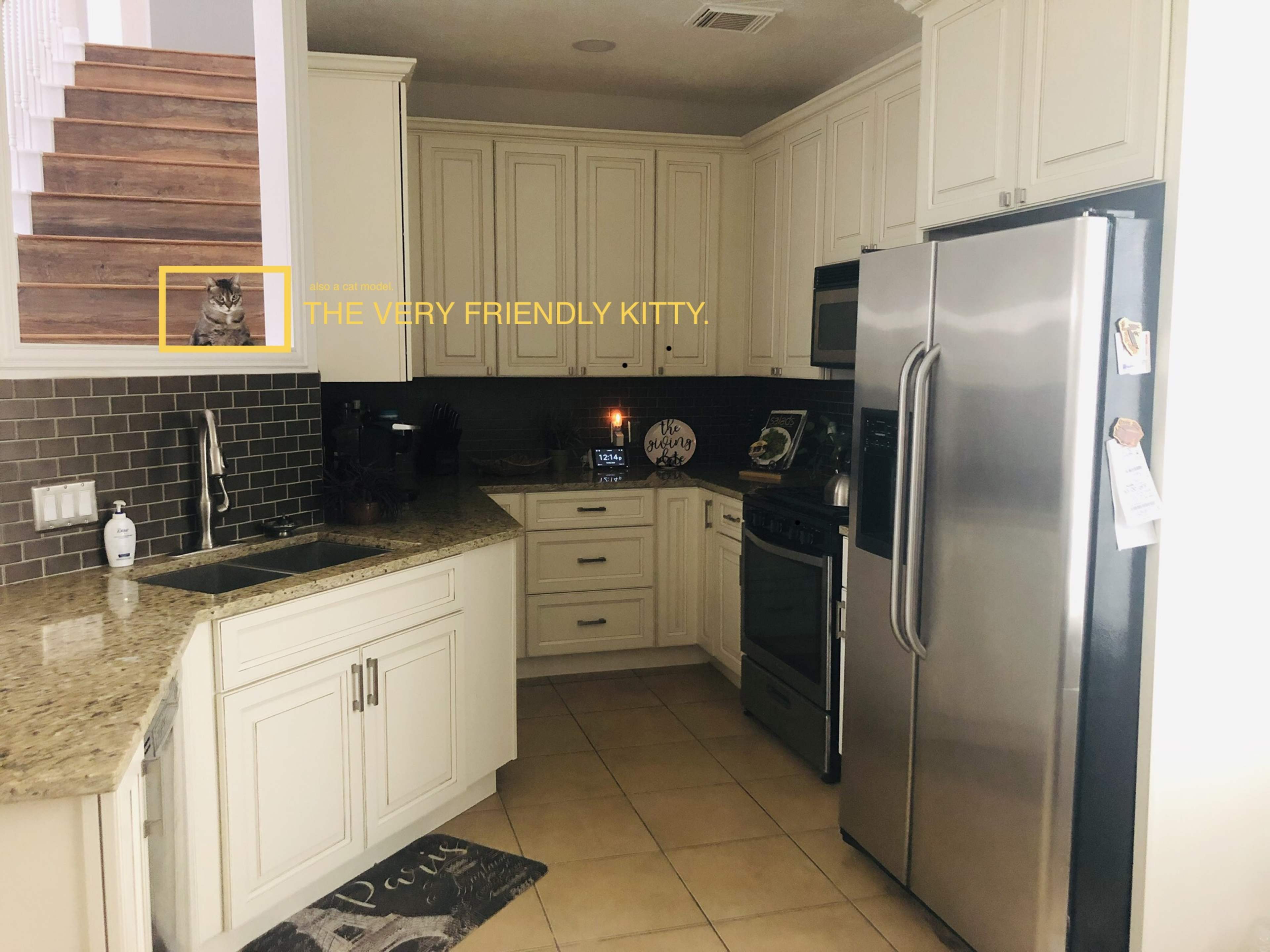 A modern kitchen features granite countertops, stainless steel appliances, and a view of a staircase in the background.