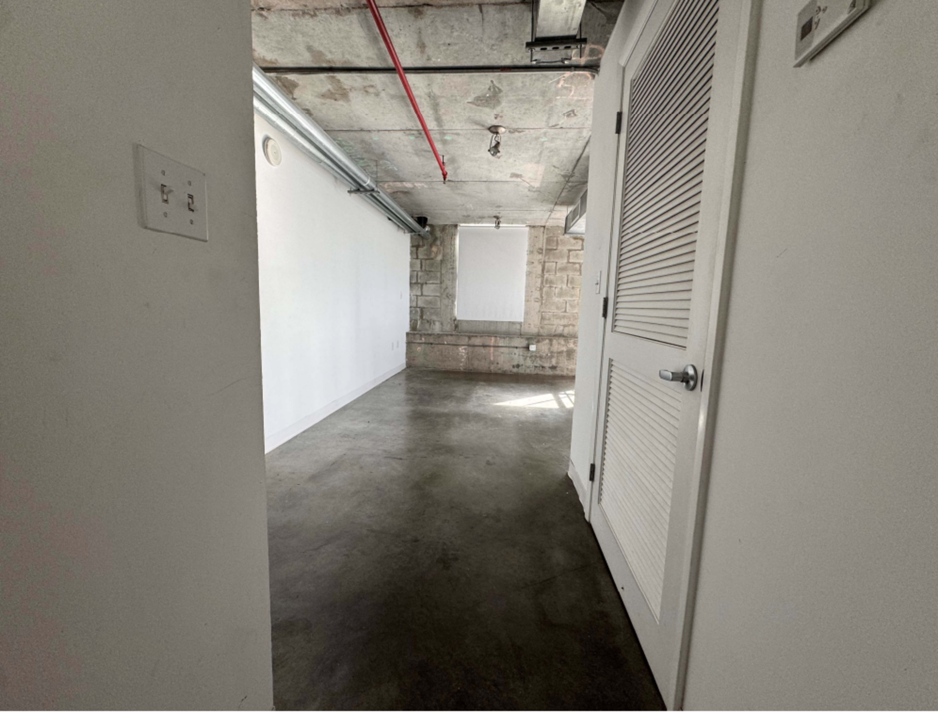 The image shows a view into a spacious, empty room with concrete floors and exposed ceiling features.