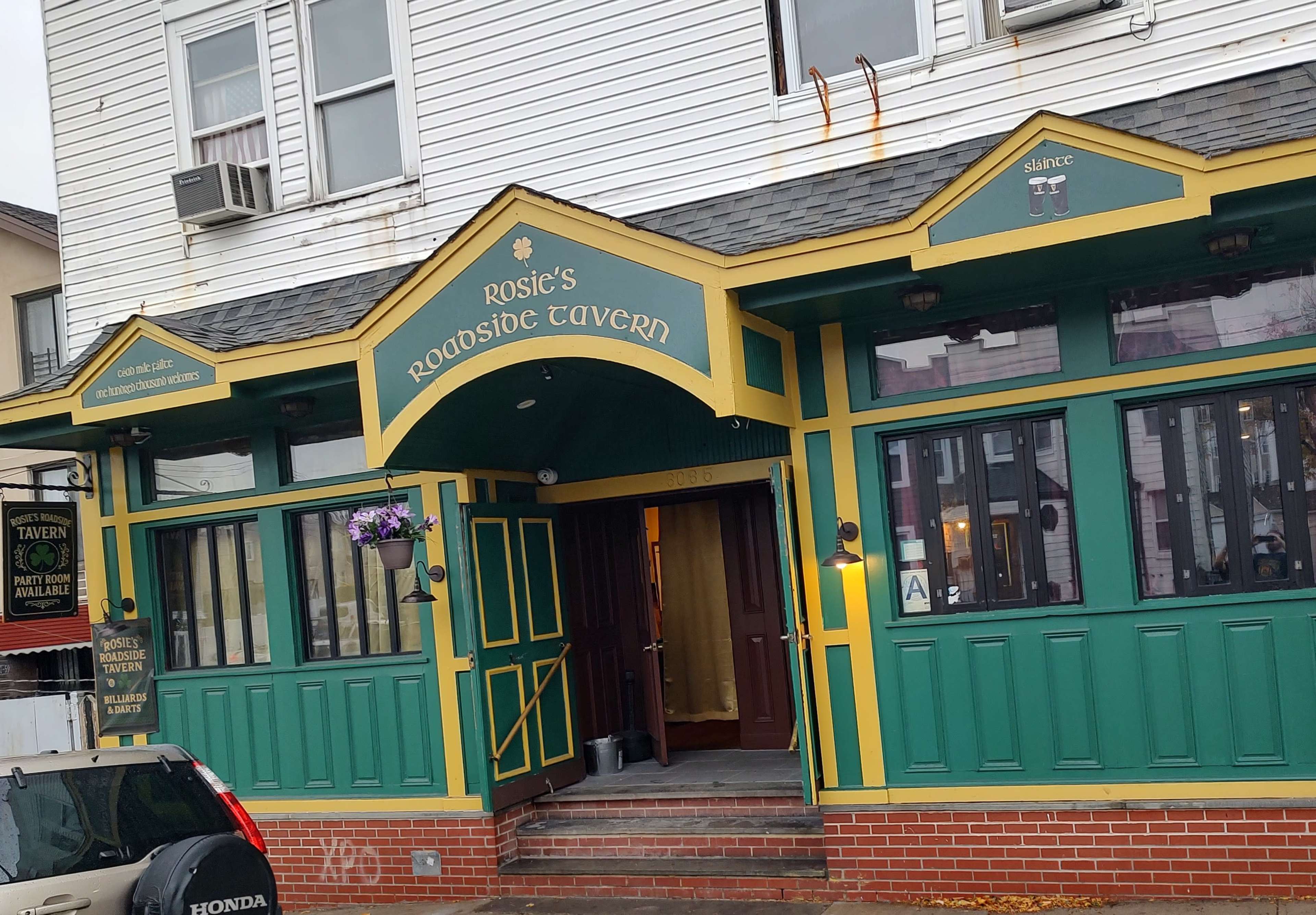 The image shows the exterior of Rosie's Roadside Tavern, featuring a green and yellow color scheme with a sign above the entrance.