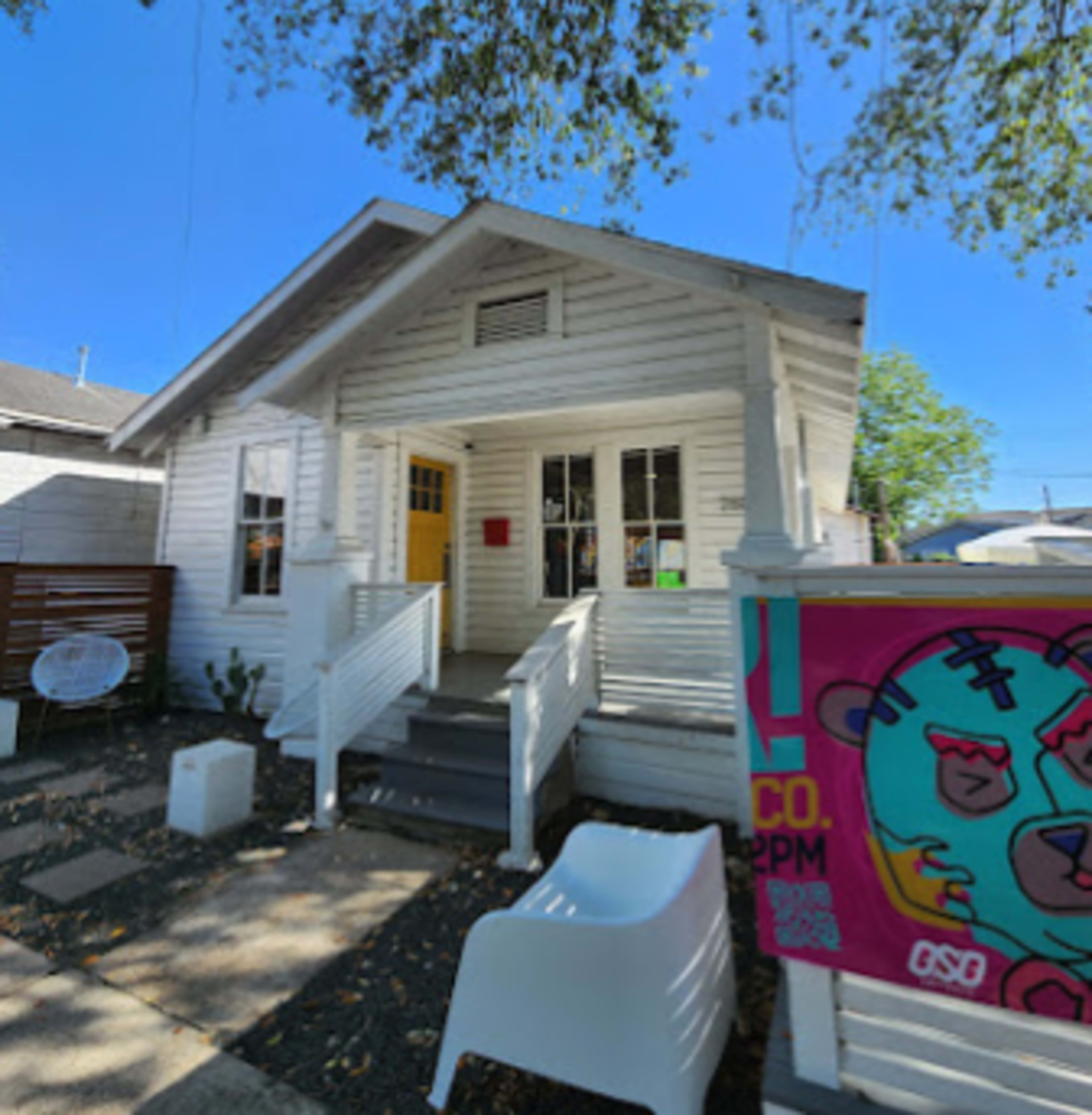 A white, single-story house with a front porch and colorful artwork displayed to the right.