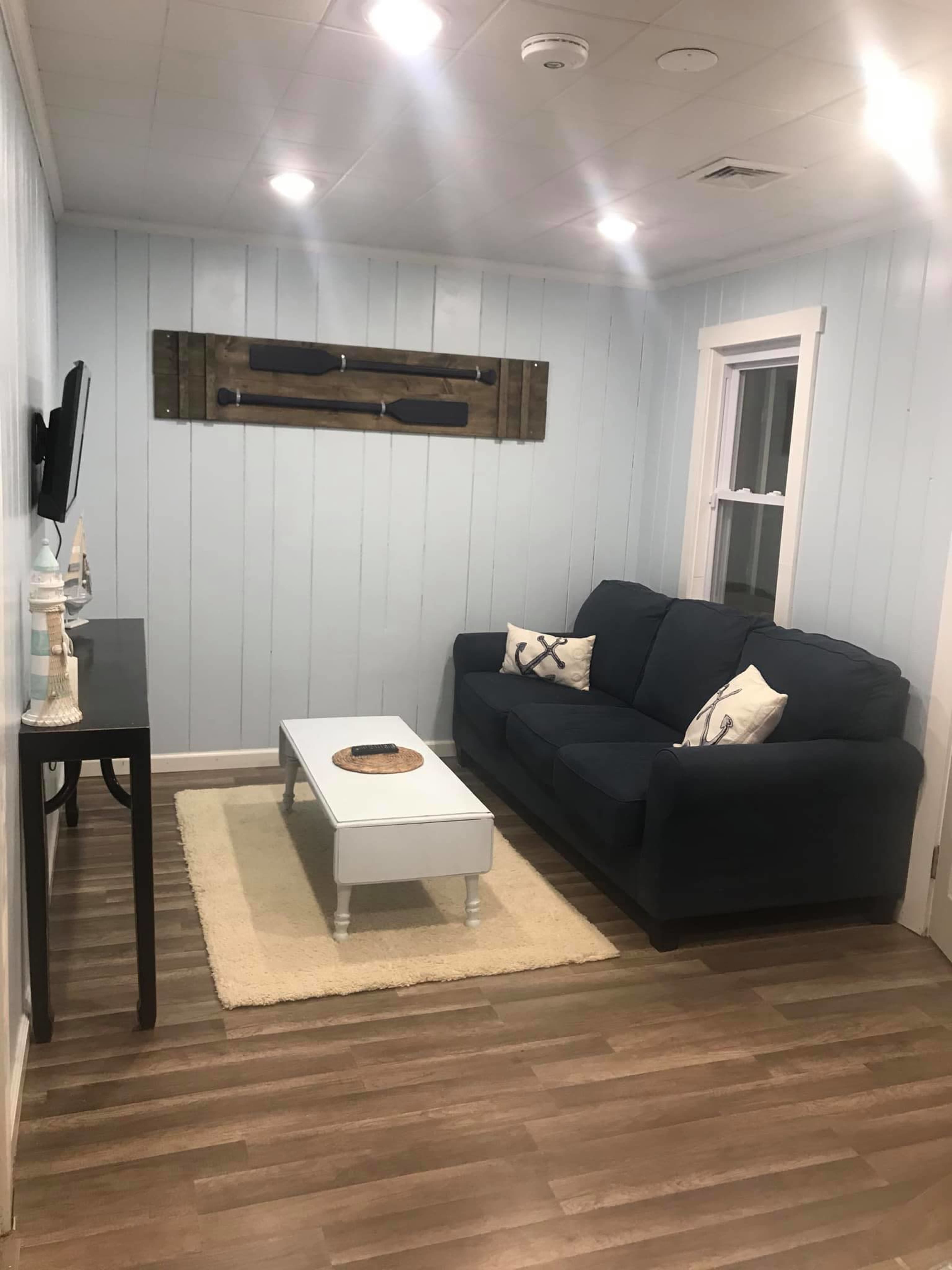 A living room with light blue walls, a dark couch, a white coffee table, and a decorative wall piece featuring two vintage-style paddles.