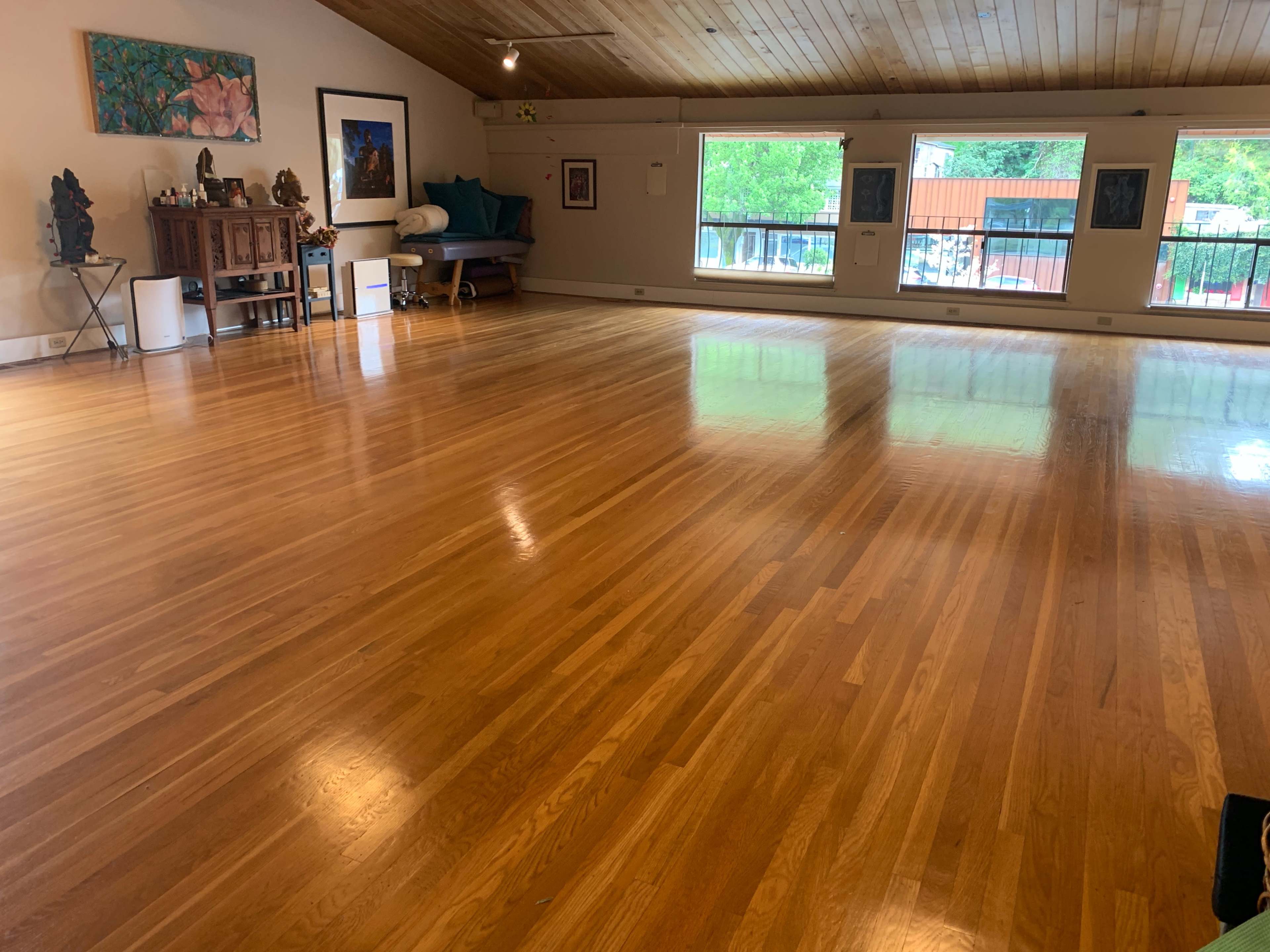 A spacious wooden-floored room with large windows and minimal furniture.