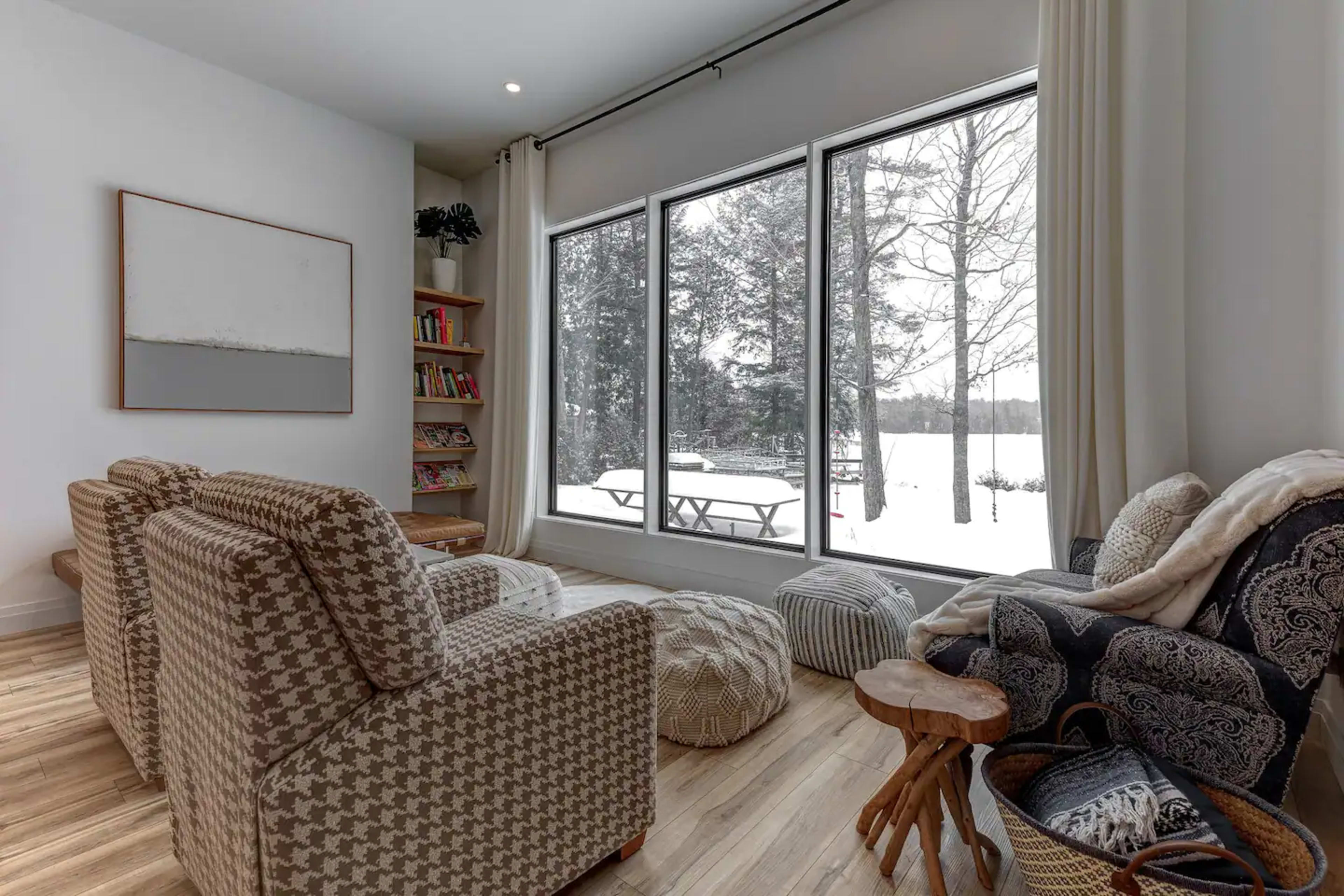 A cozy living room with two patterned armchairs, a small wooden table, and large windows overlooking a snowy landscape.