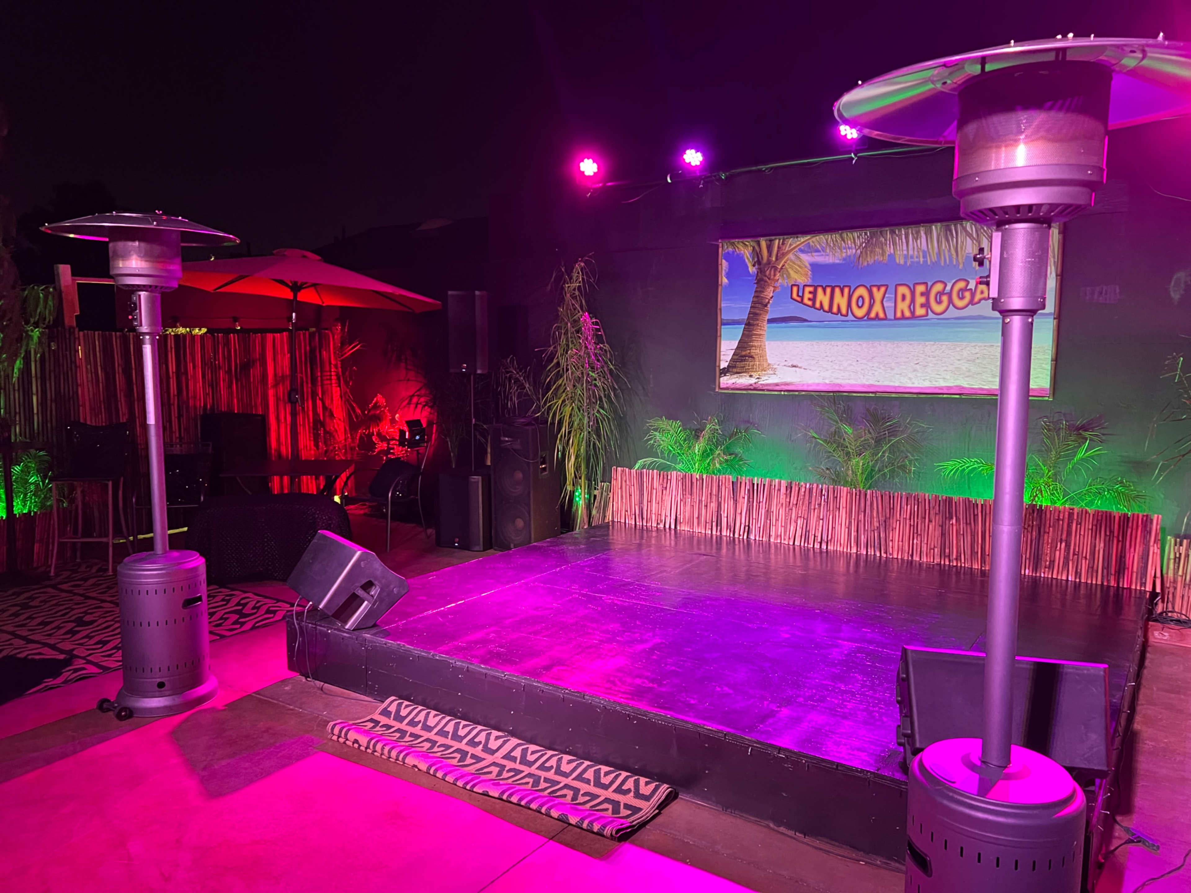 A stage setup with two patio heaters, surrounded by colorful lighting, and a backdrop featuring a sign that reads "CennoX Reggae."