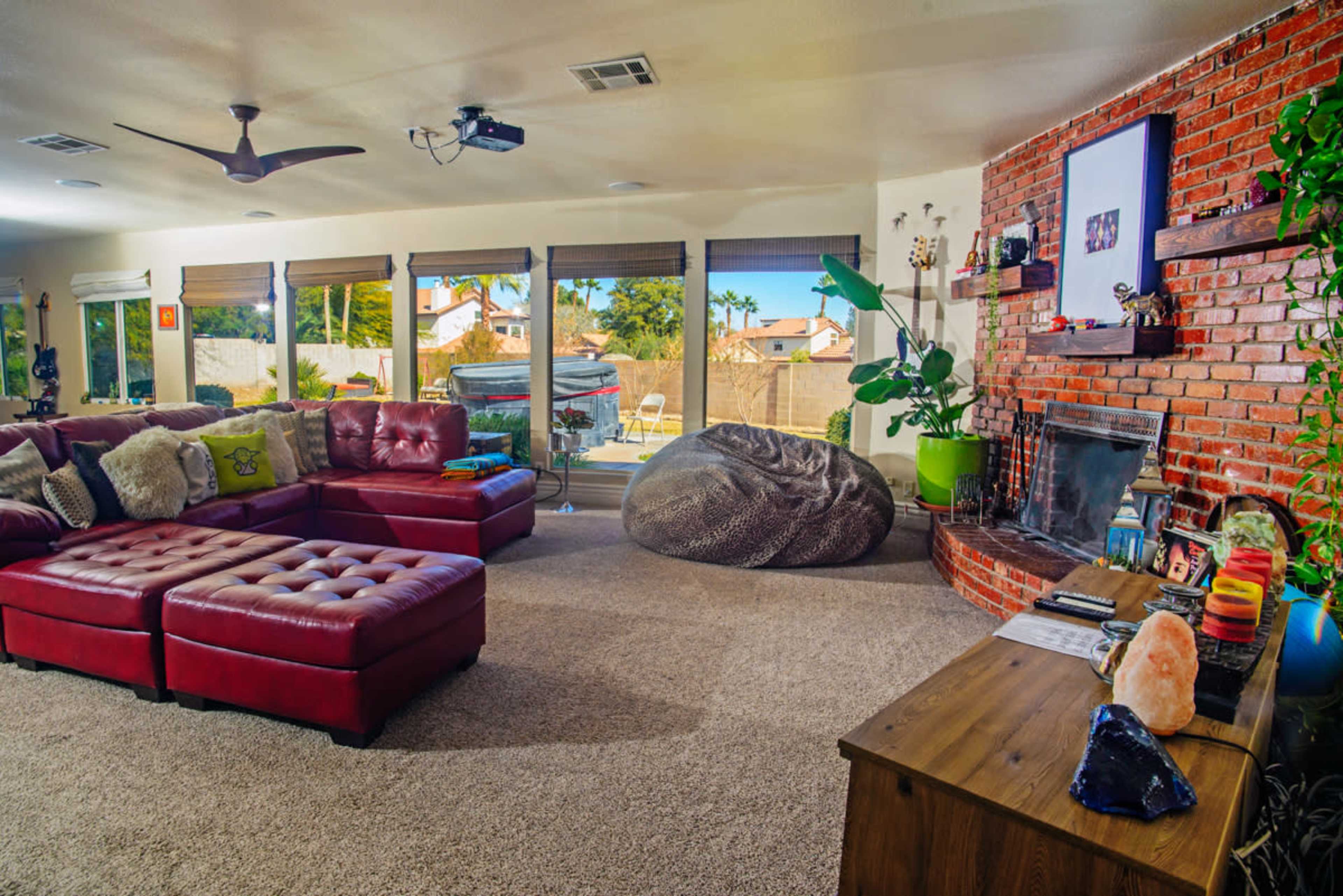 A spacious living room features a large red sectional sofa, a bean bag chair, and a brick fireplace, with windows overlooking a backyard.