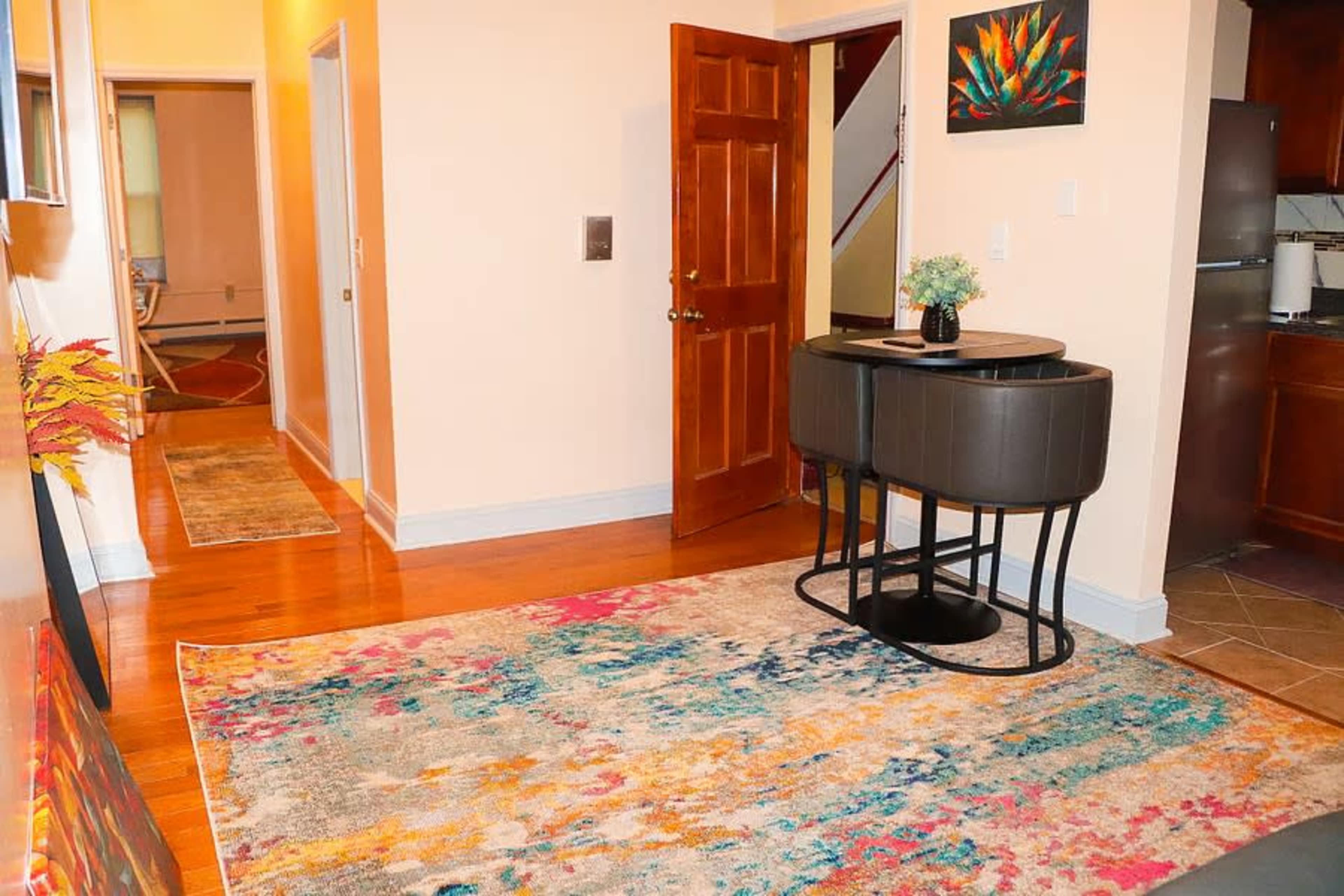The image shows a bright entryway with a colorful rug, a small console table, and doors leading to different areas of the home.