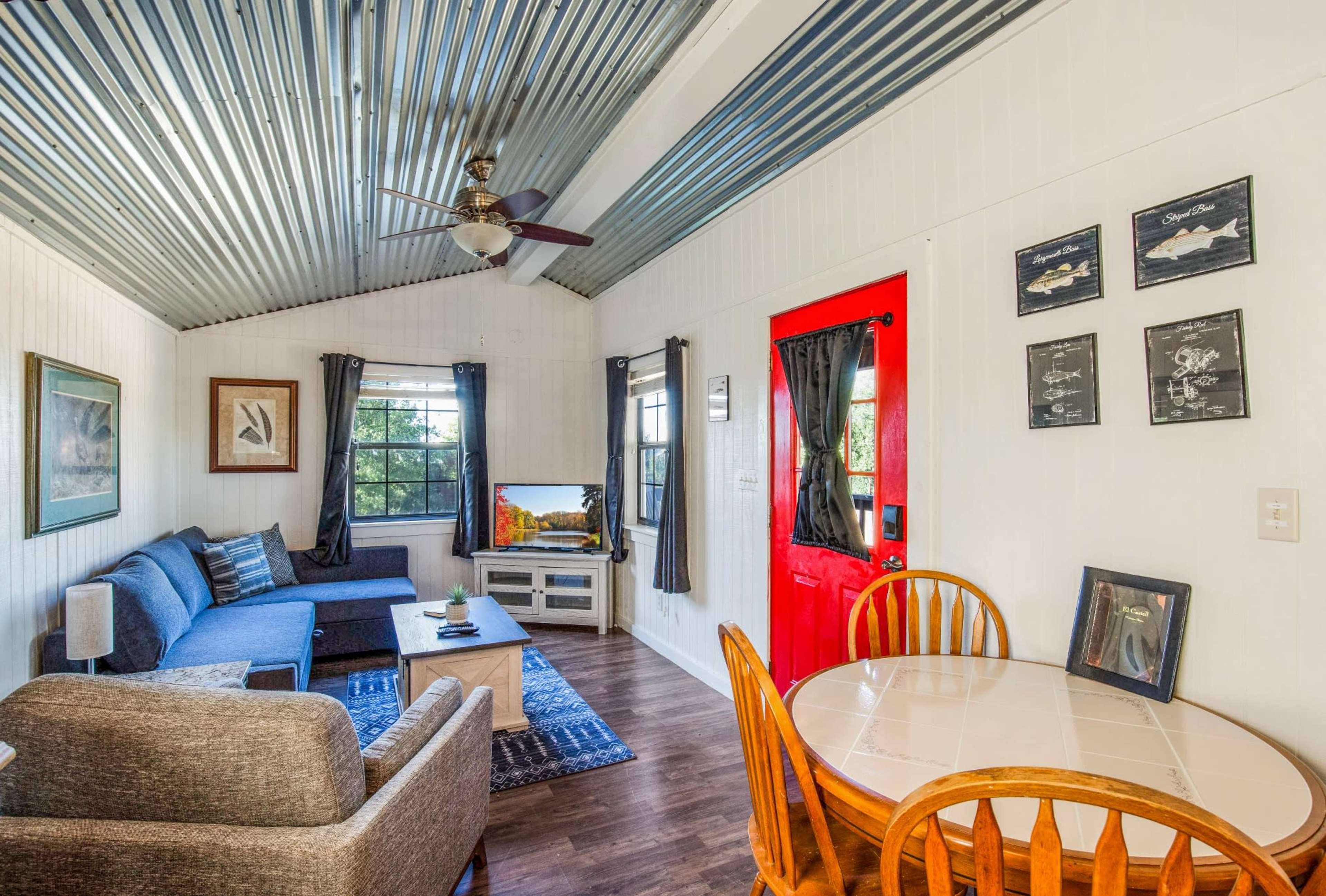 A small living area features a gray sofa, a round dining table, and a bright red front door.