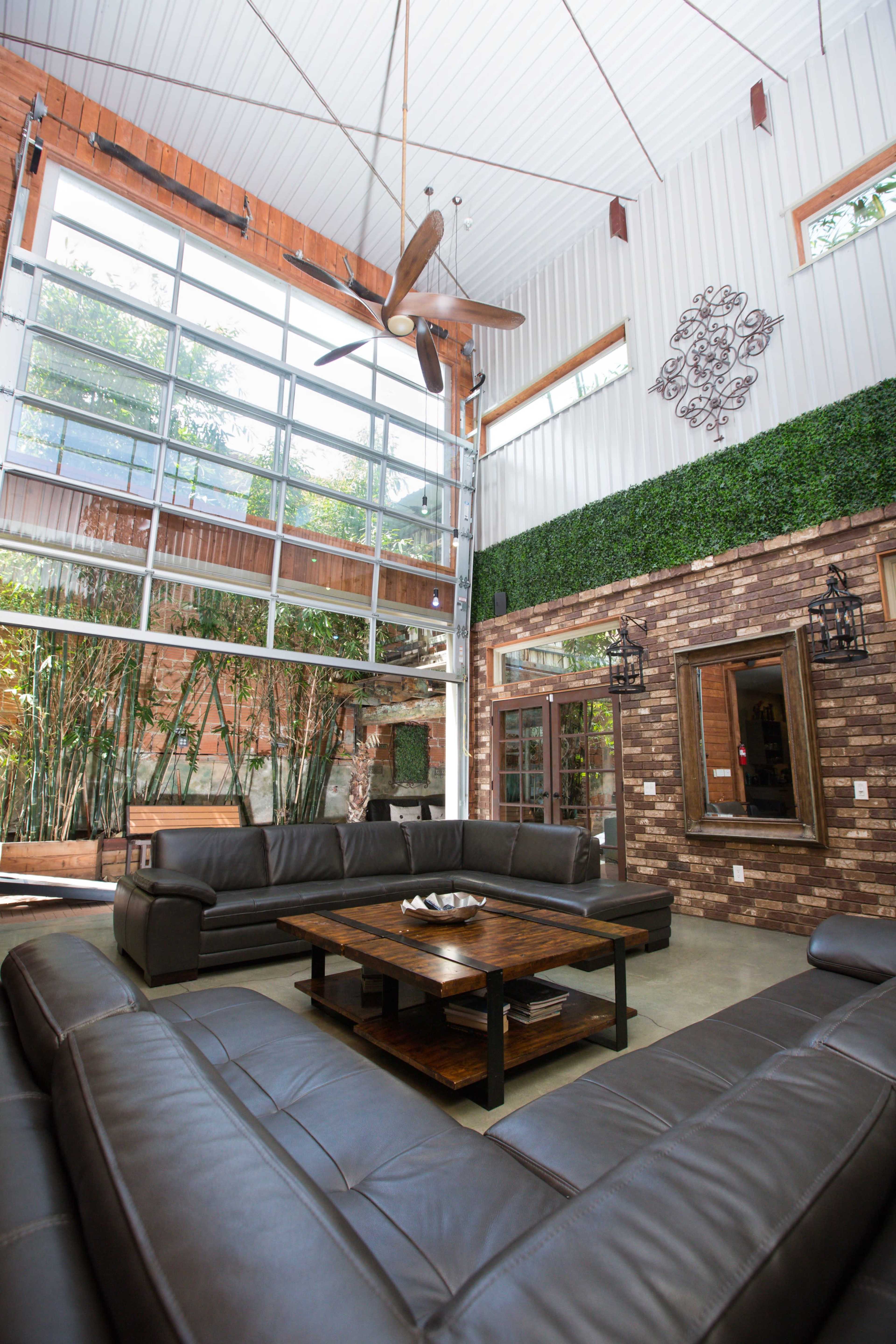A spacious living room with a high ceiling, large windows, and modern furnishings arranged around a central coffee table.