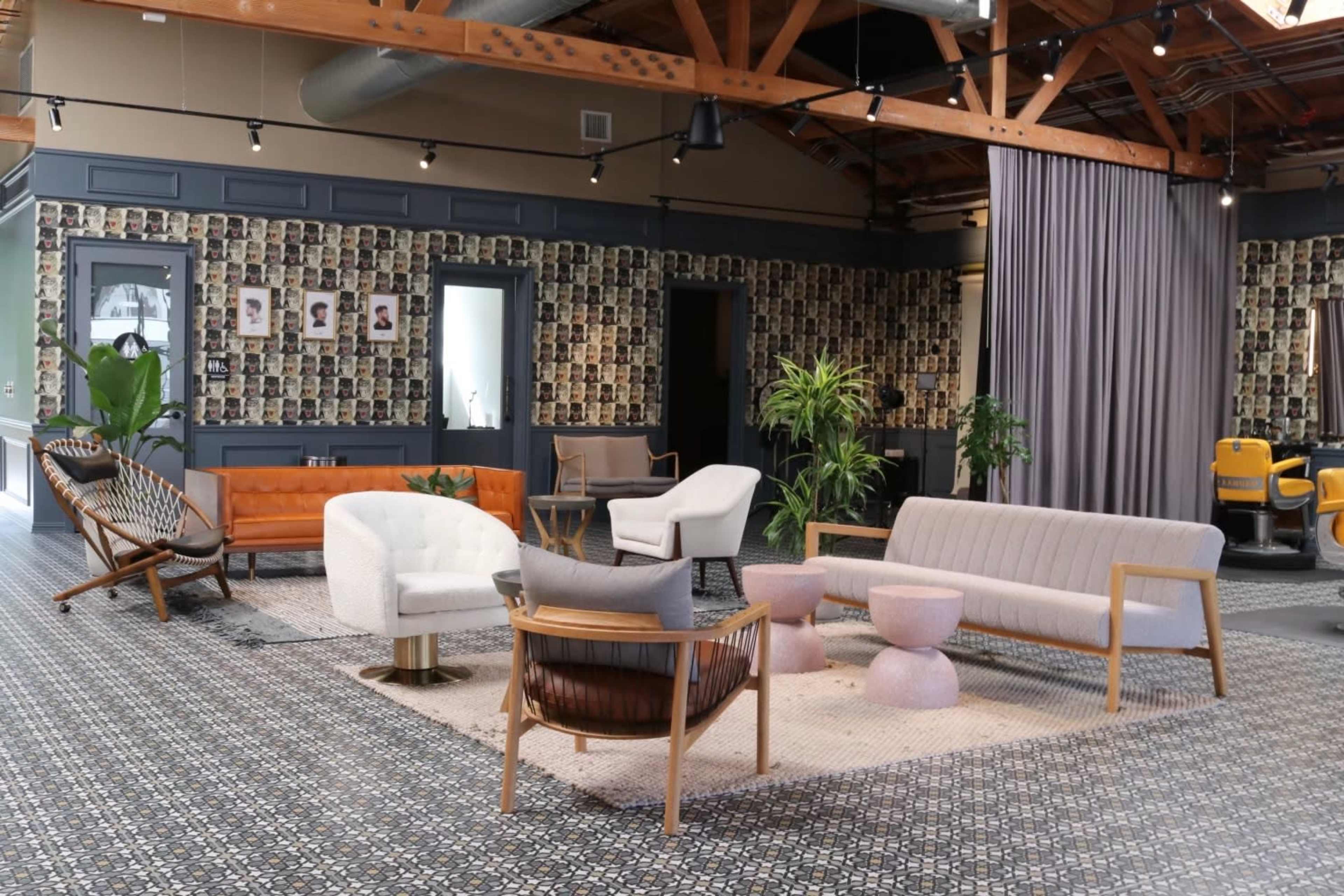 A modern lounge area featuring a mix of seating options, including a gray sofa, white chairs, and a wooden armchair, set against a wall decorated with numerous framed photographs.