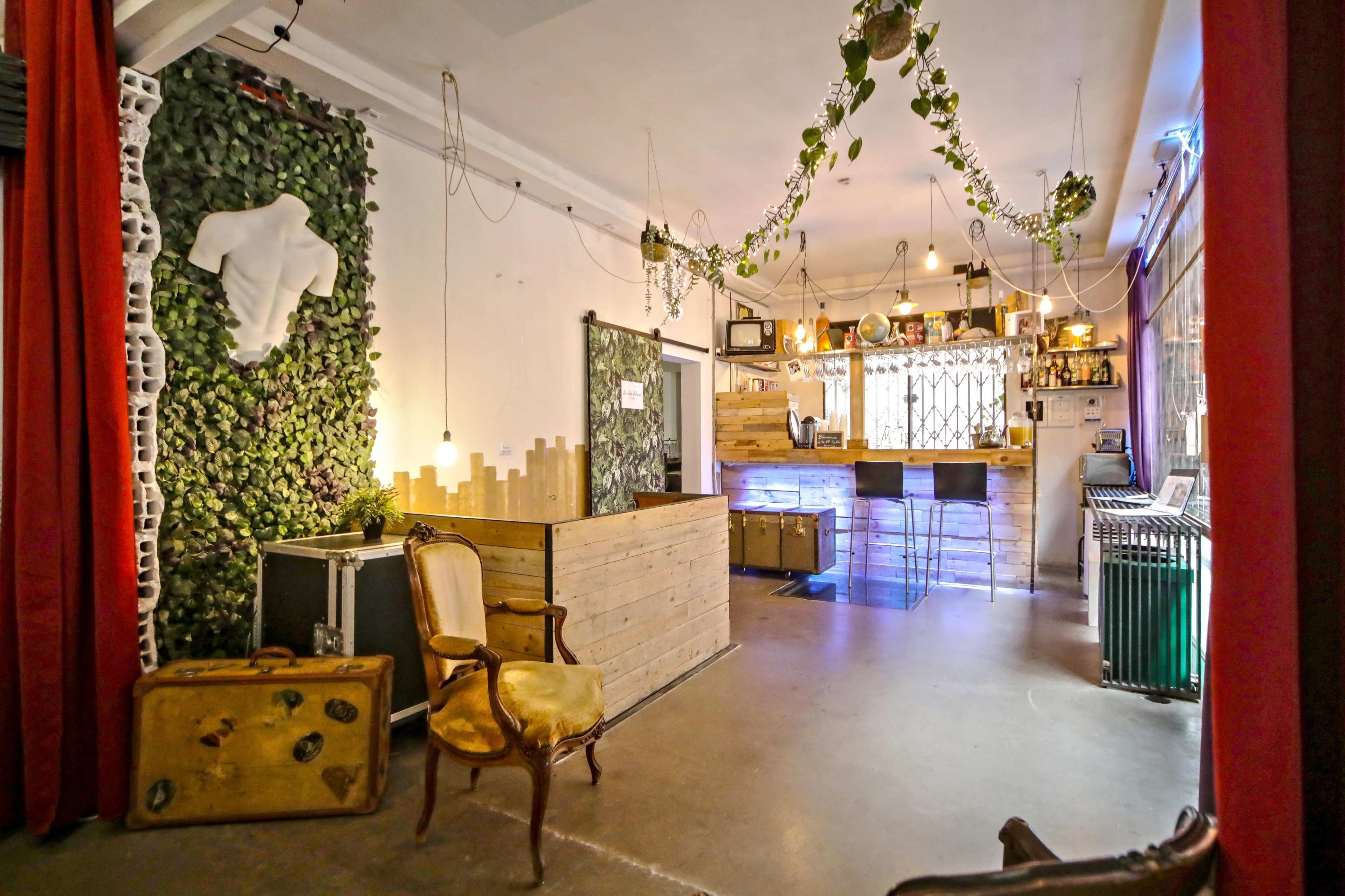 An interior space with a bar area, wooden counter, and greenery on the walls, illuminated by pendant lights.