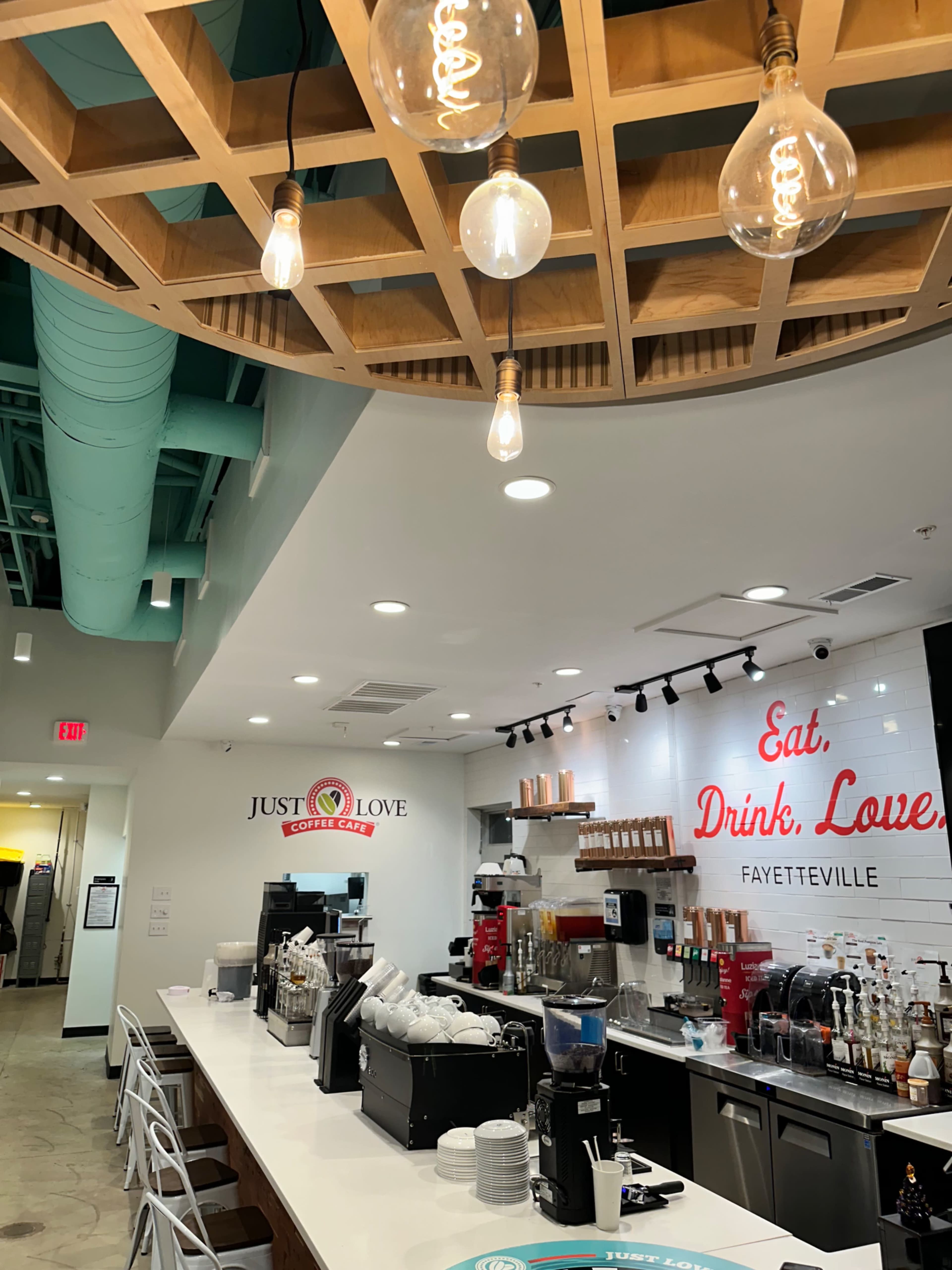 The interior of a coffee shop with a modern design, featuring a long counter with coffee equipment and a bright chandelier overhead.