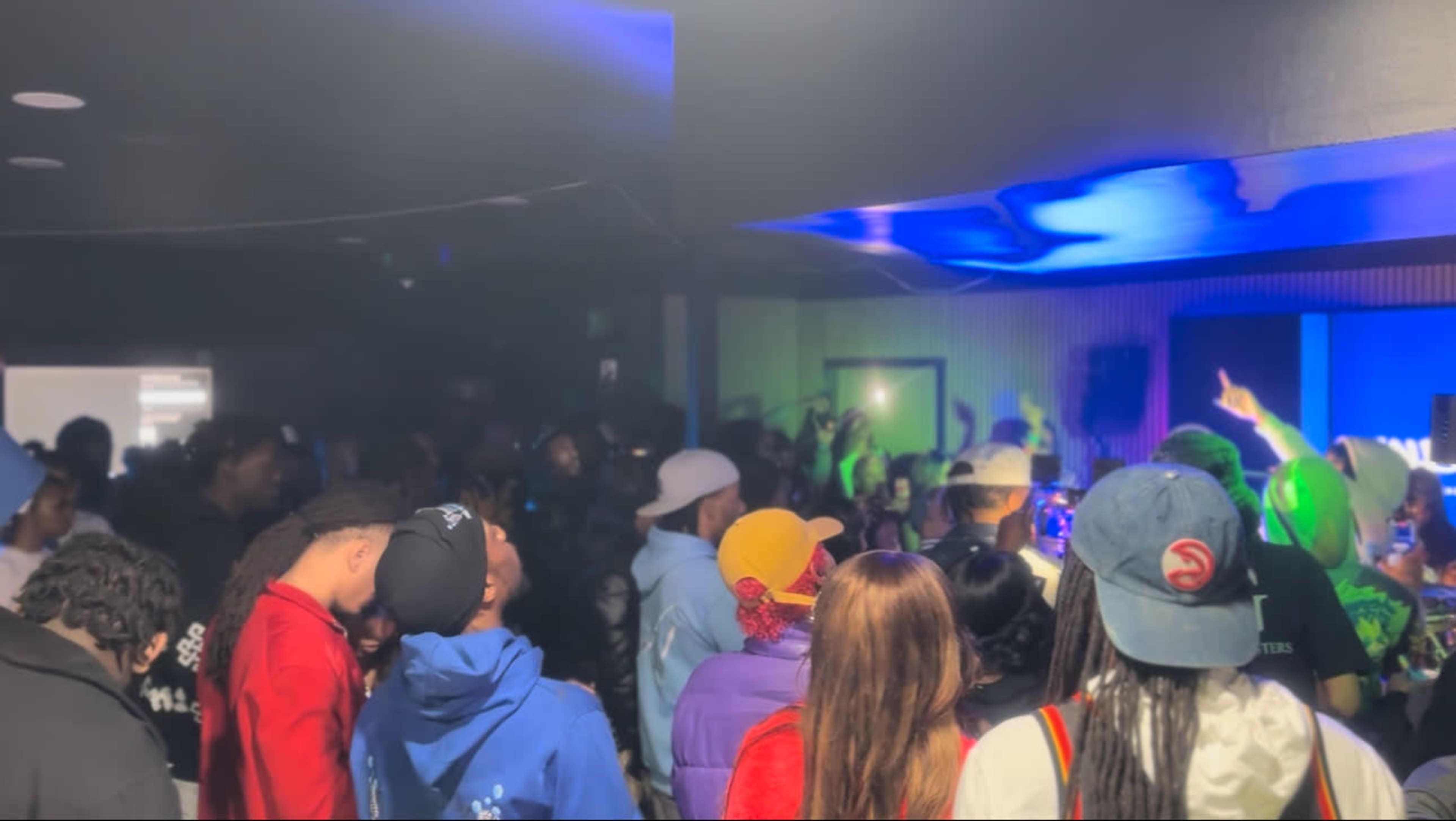 A crowd of people gathers in a dimly lit venue, focusing on a performance taking place on stage.