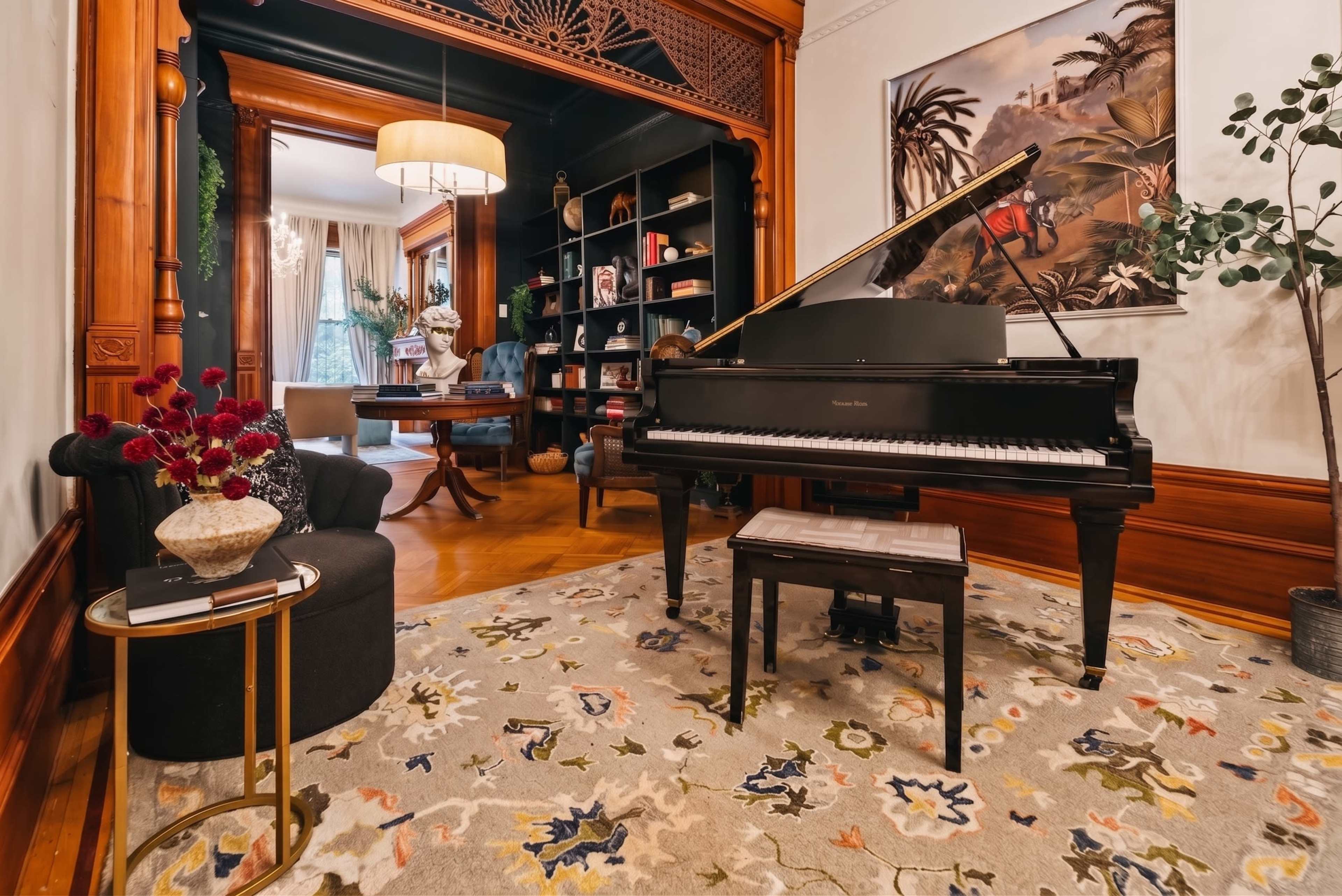 A grand piano is positioned near a plant and a small table, with a decorative rug covering the wooden floor in a well-furnished room.