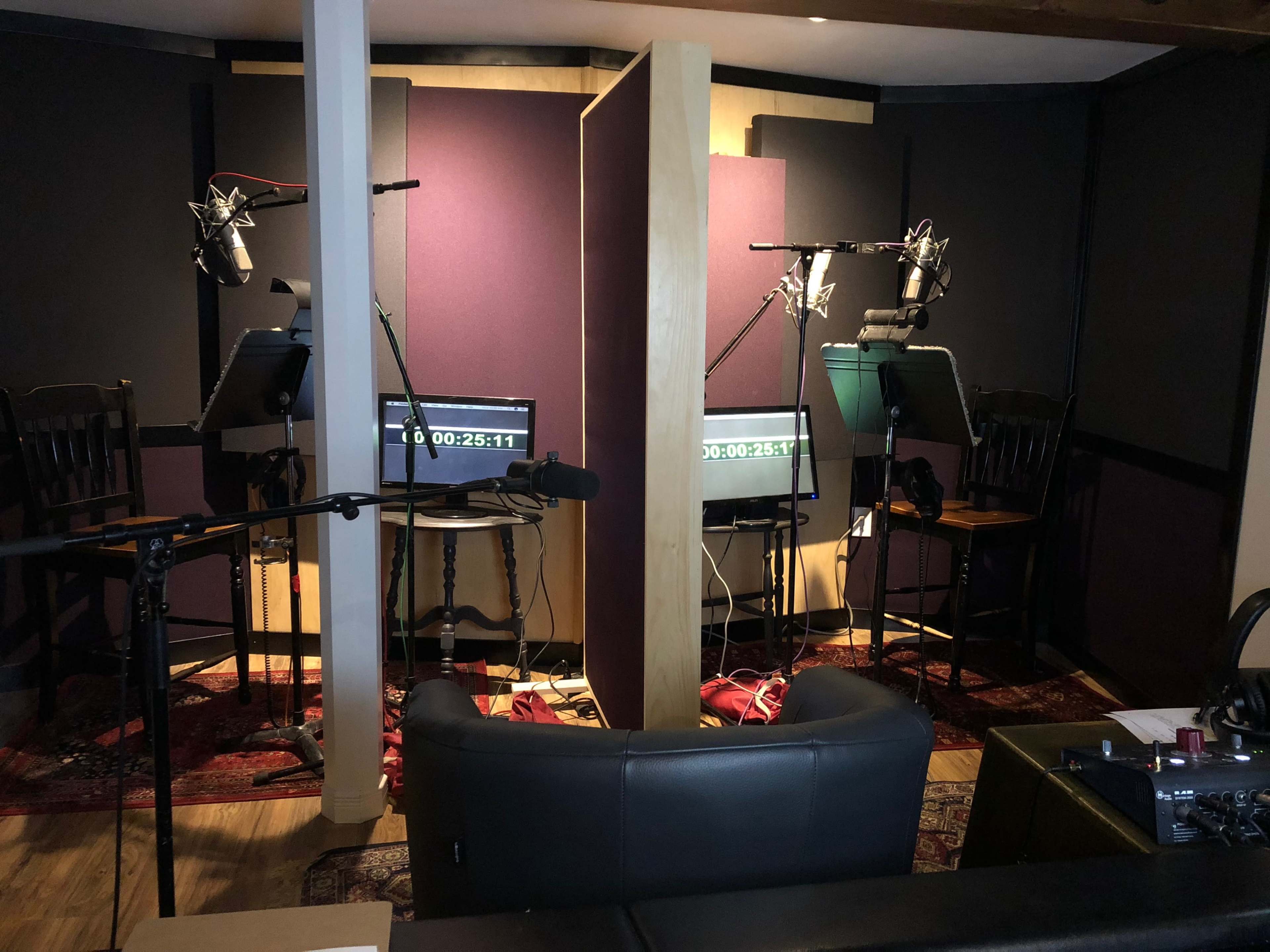 A sound recording studio with two separate vocal booths, each containing microphones and monitors, divided by a central partition.