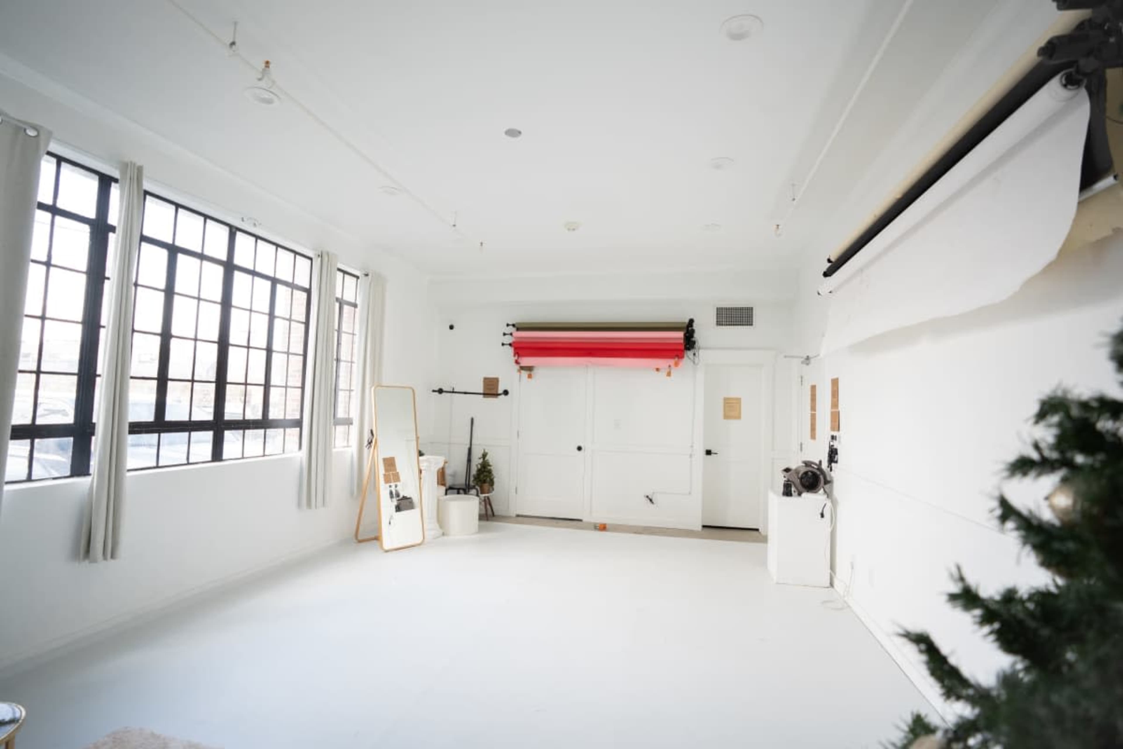 The image shows a bright, spacious studio with white walls, large windows, and a backdrop roll system against one wall.