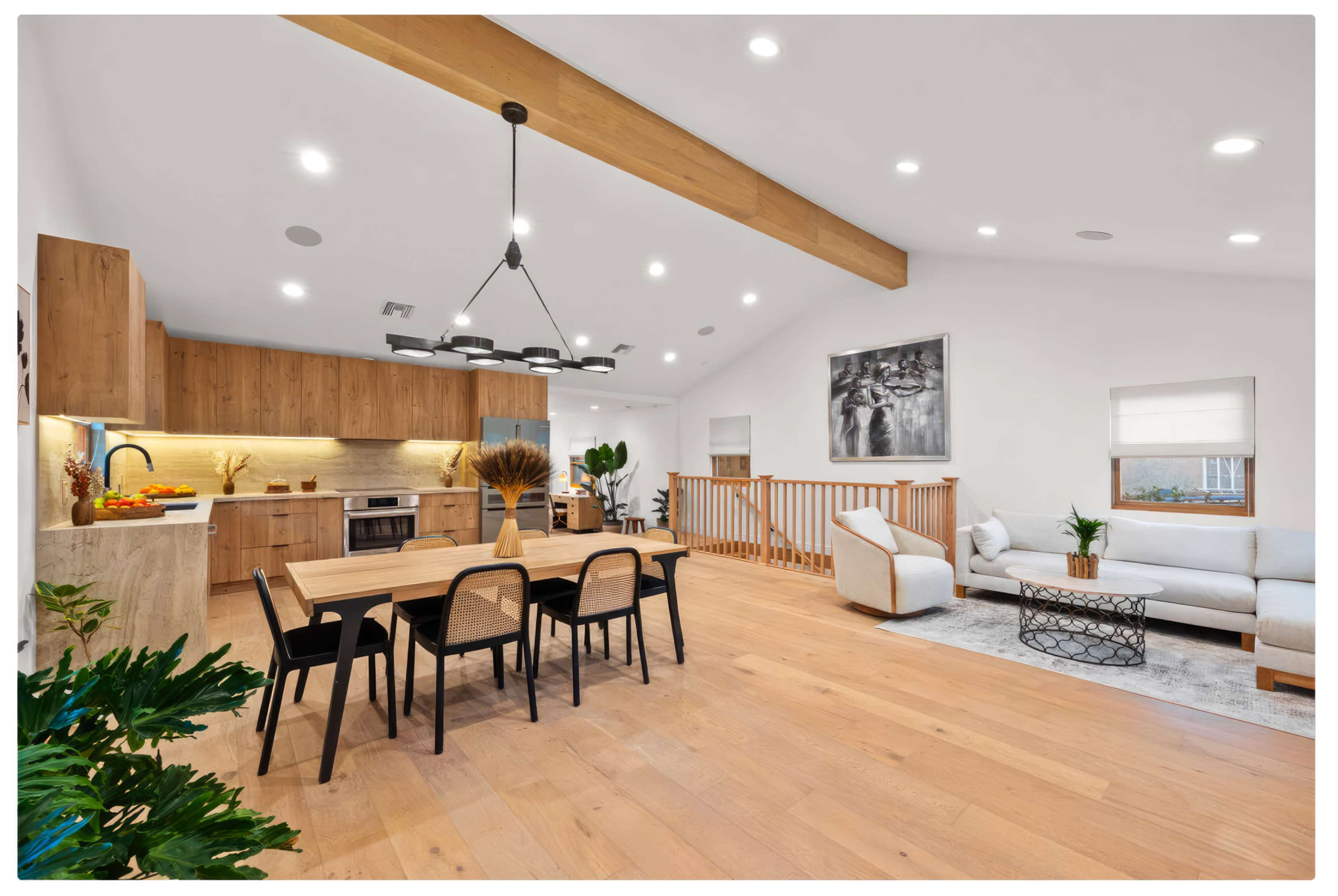 A spacious, modern living area features a dining table, a kitchen with wooden cabinetry, and a comfortable seating area with light-colored furniture.