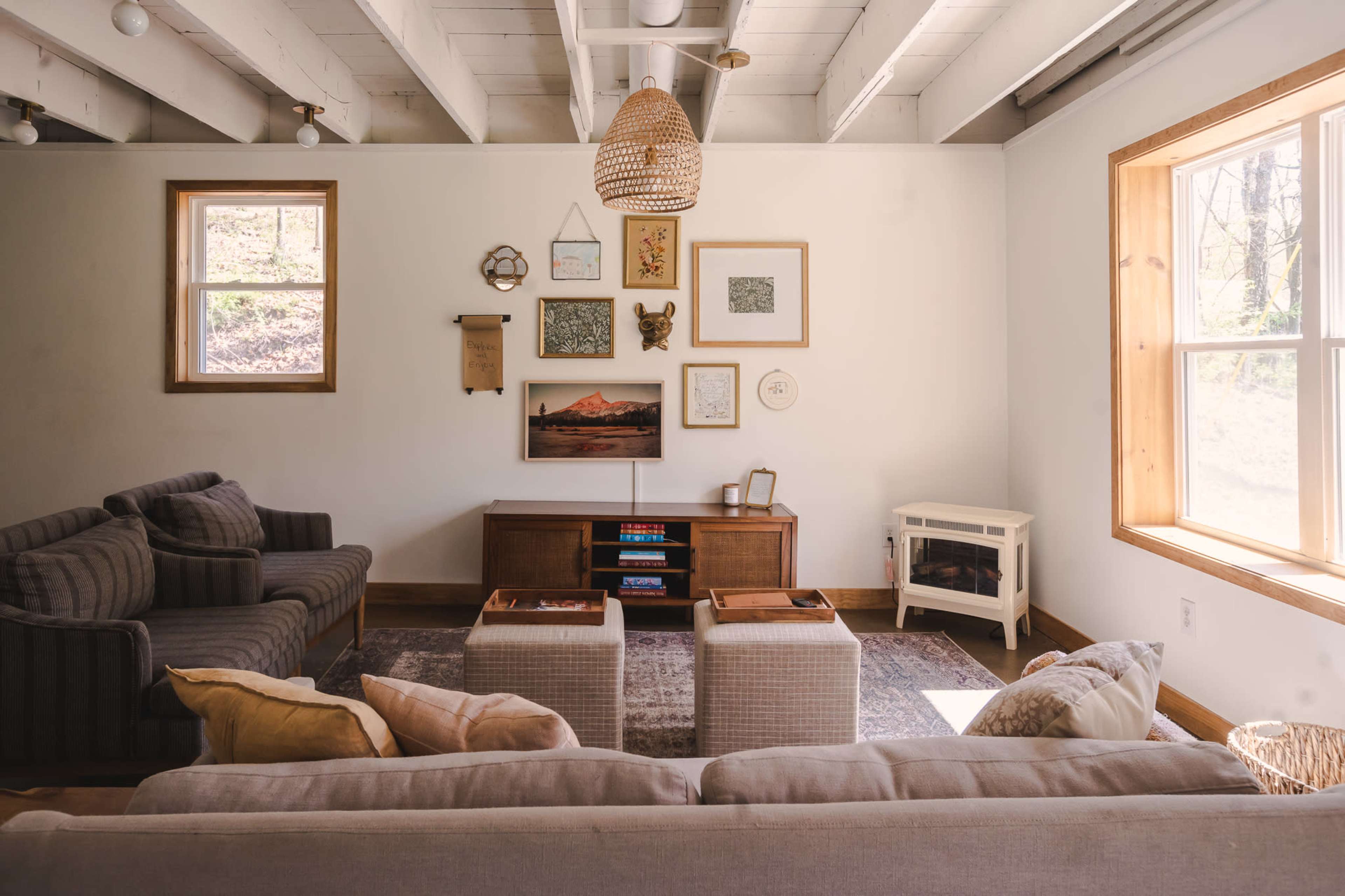 The living room features two sofas, a wooden coffee table, and a wall adorned with various framed artworks, illuminated by natural light from two windows.