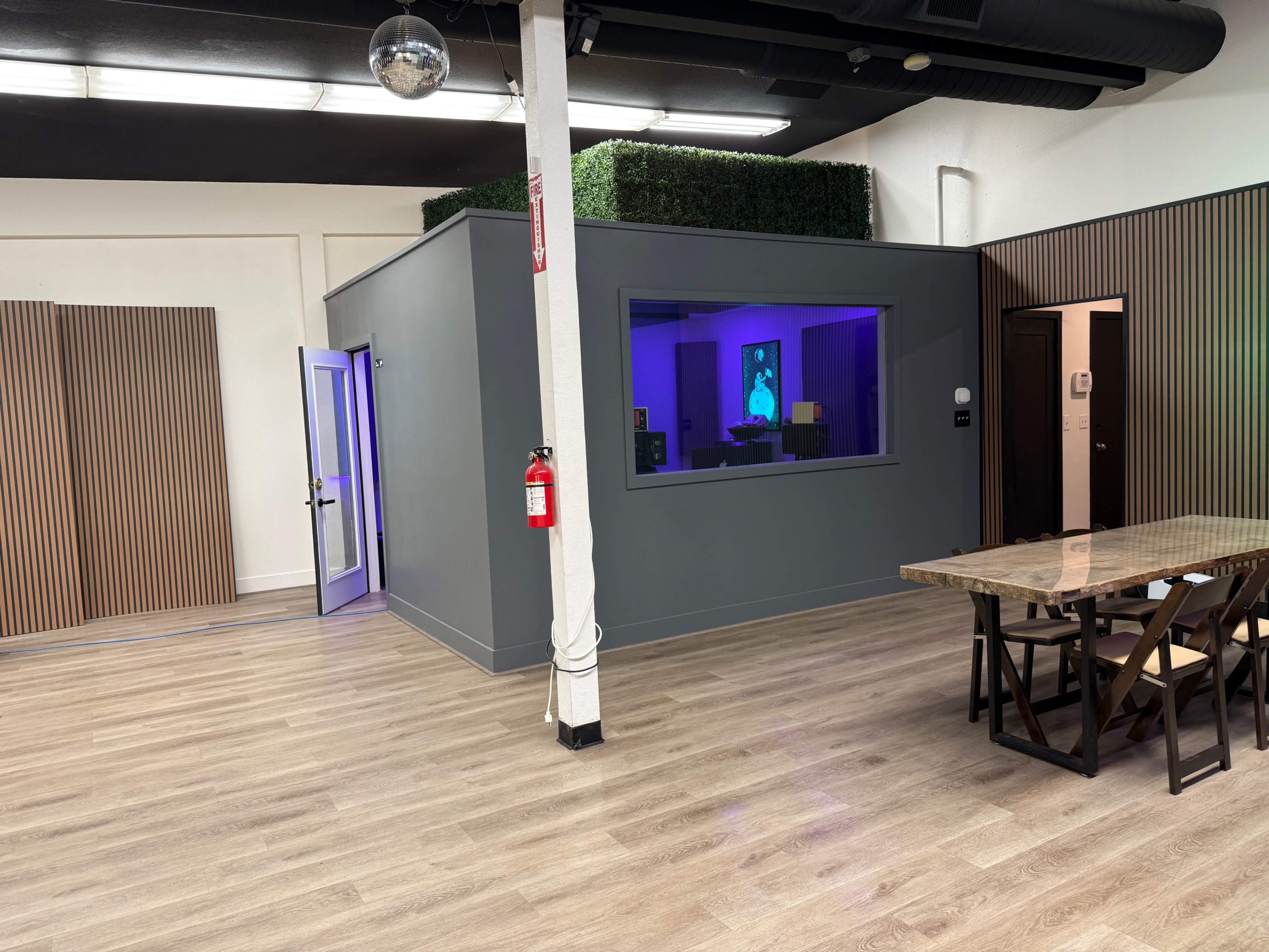 The image shows a modern office space featuring a gray meeting room with a large window, wooden paneling on one wall, and a long table with chairs nearby.