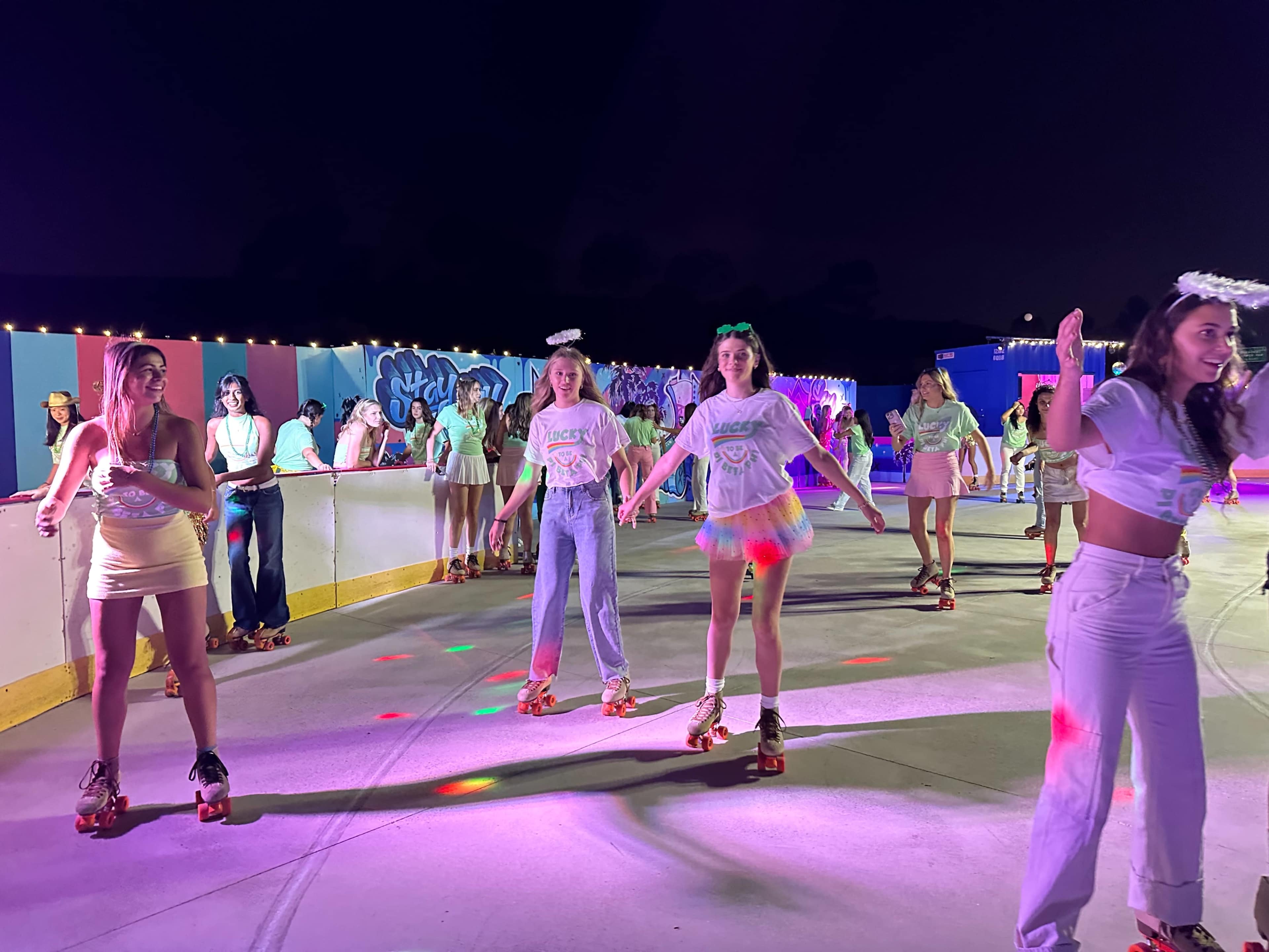 A group of people roller skate on a brightly lit rink surrounded by colorful decorations at night.