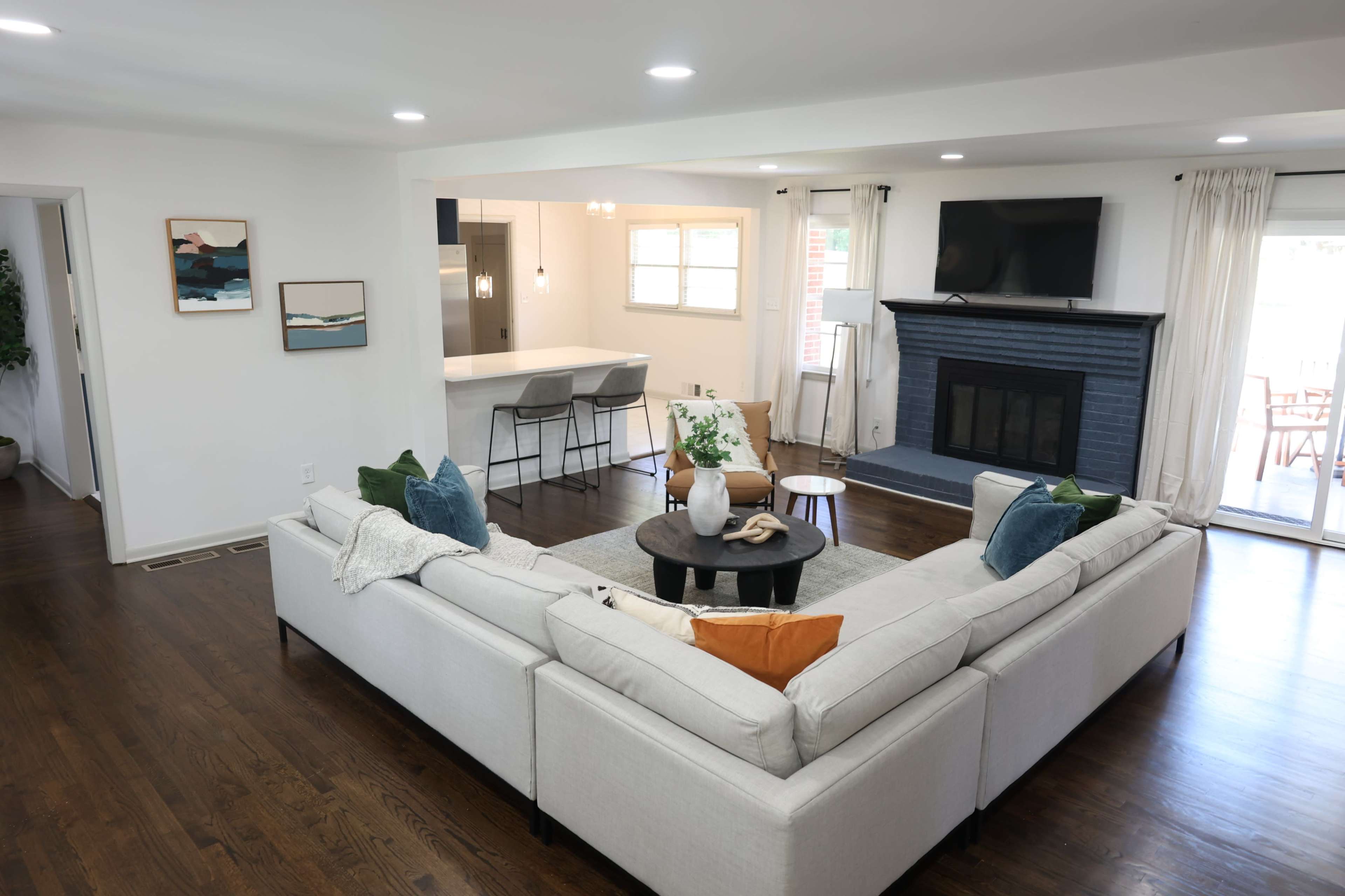 A spacious living room features a large L-shaped sectional sofa, a round coffee table, and a fireplace, with natural light streaming through the windows.