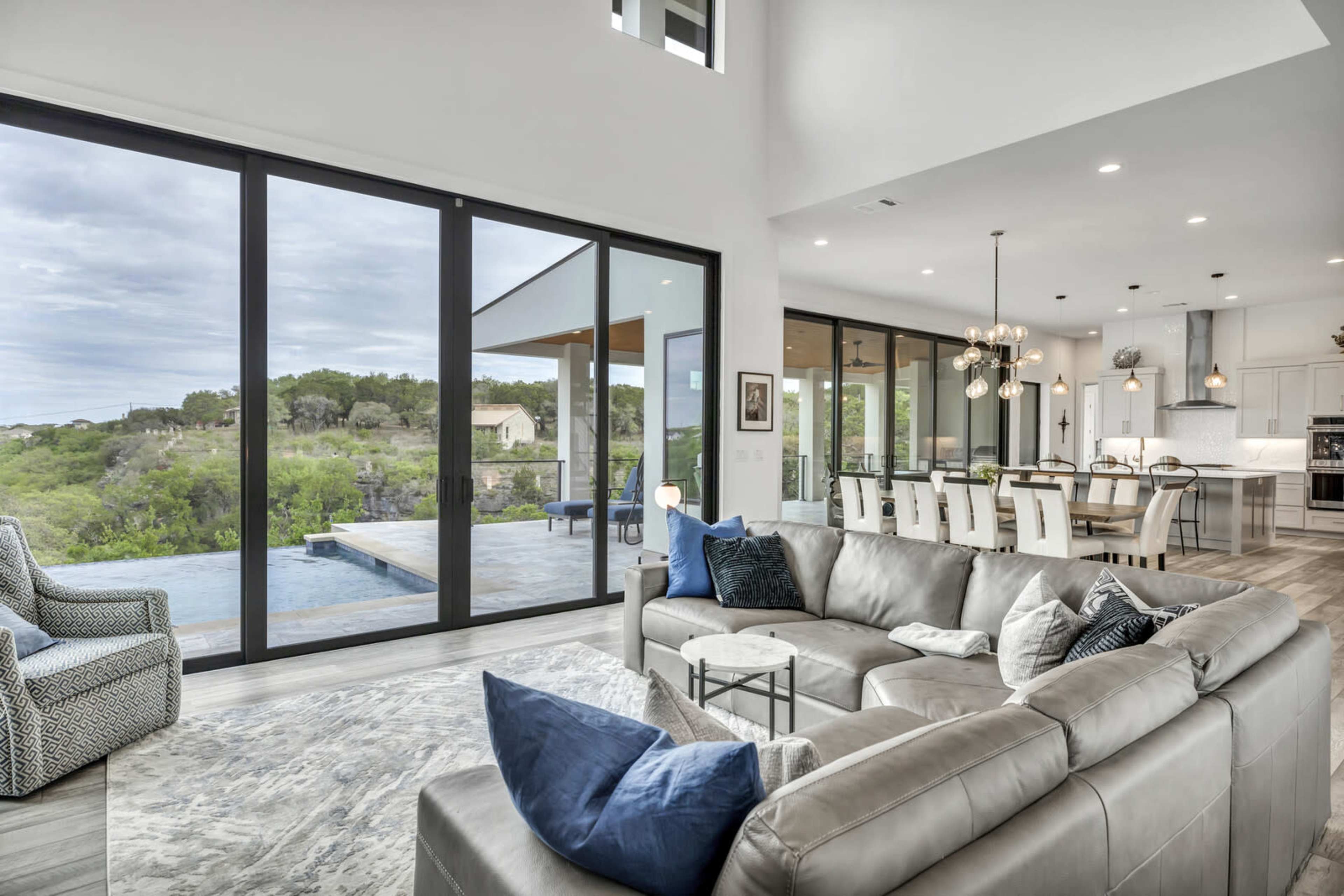 A modern living room with large windows overlooking a green landscape and a pool area.