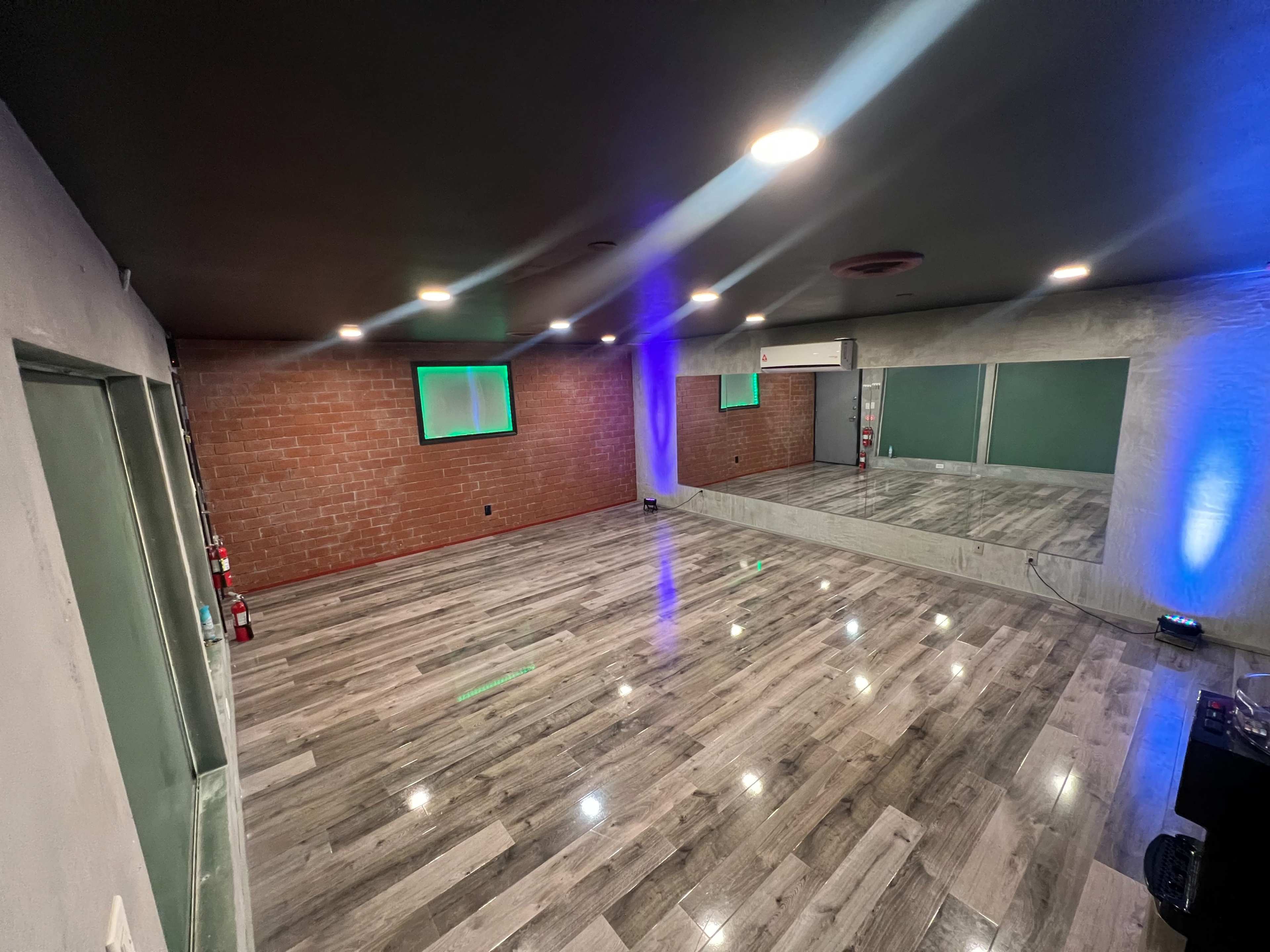 A spacious interior room with hardwood flooring, exposed brick walls, and large mirrors on one side.